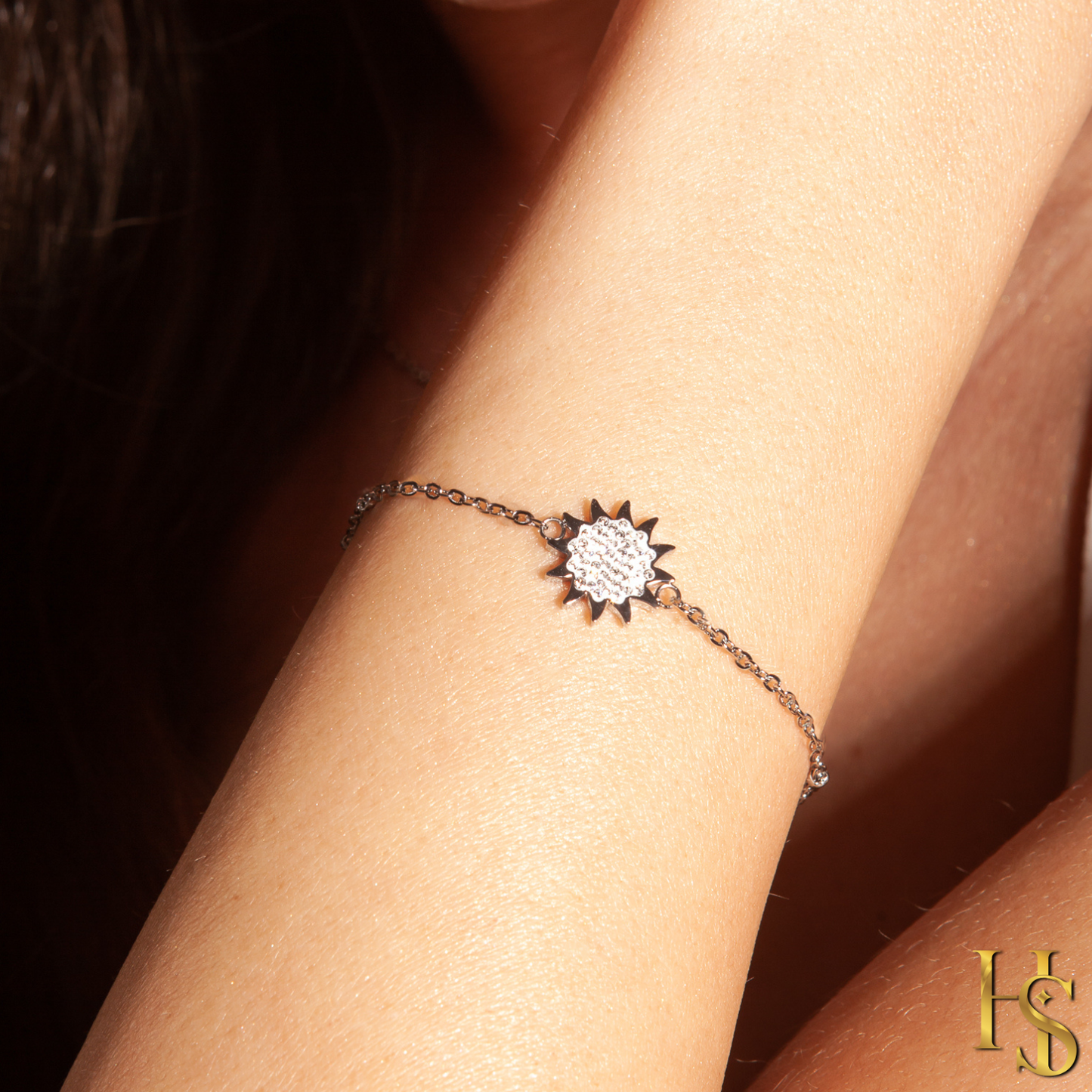 A sterling silver chain bracelet with a sun charm paved with American diamonds, worn on a model's wrist.