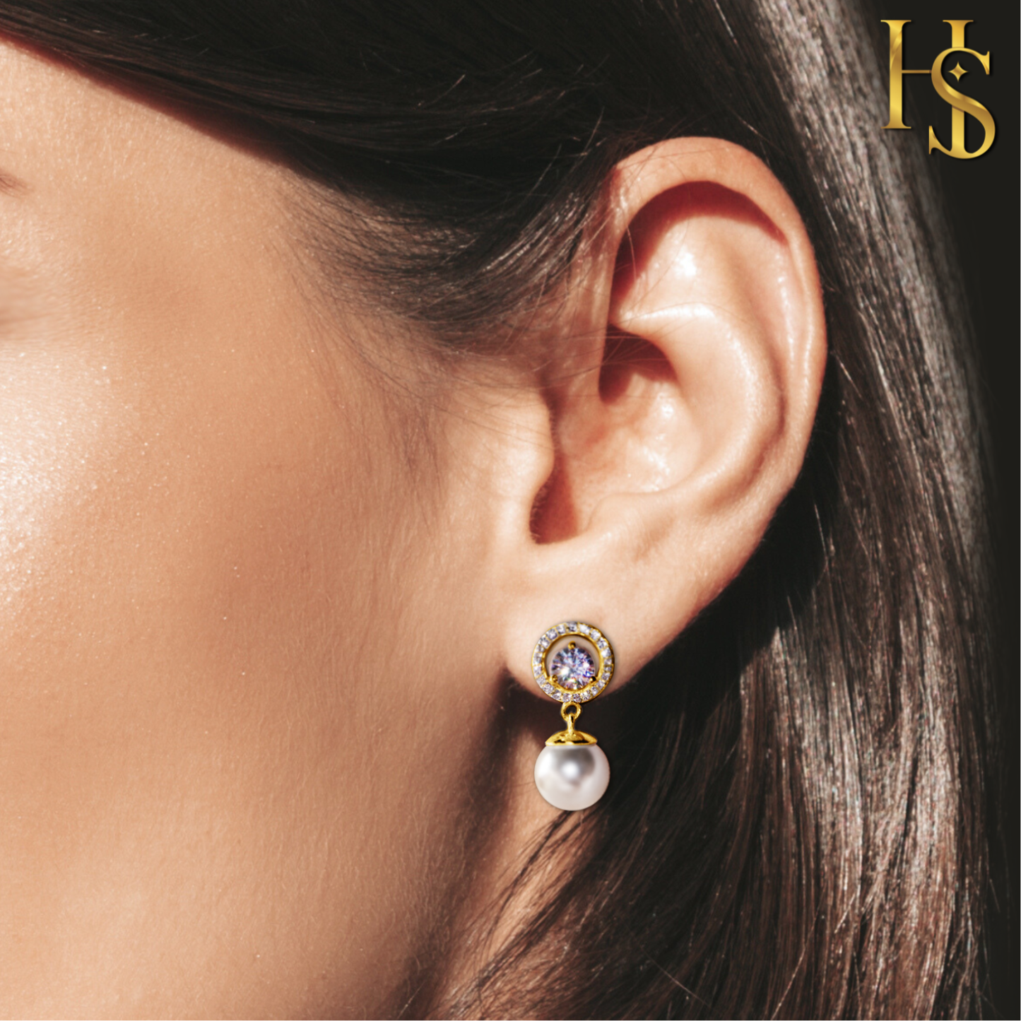 Gold-plated drop earrings with a central purple stone in a halo of American diamonds and a dangling white pearl, worn on the ear.