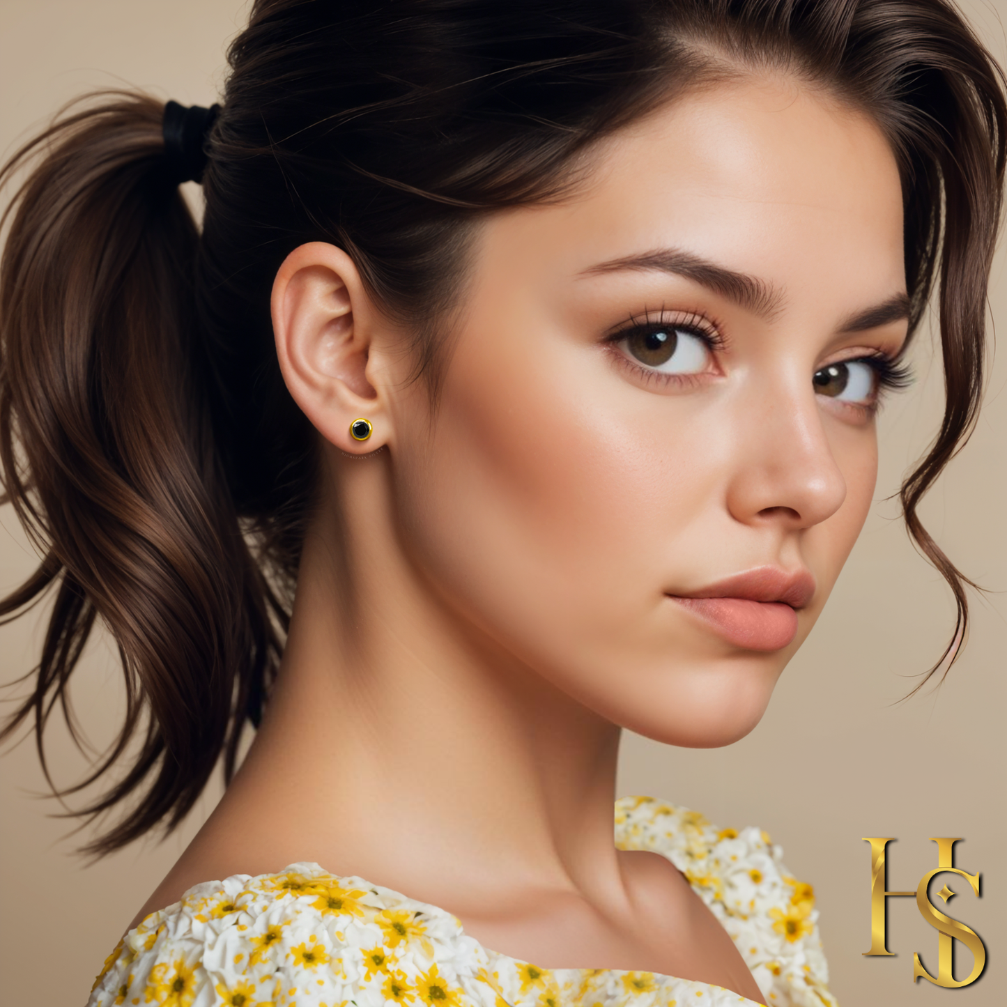A round black solitaire stud earring in a gold-plated bezel setting, worn on the ear of a model with her hair in a ponytail.