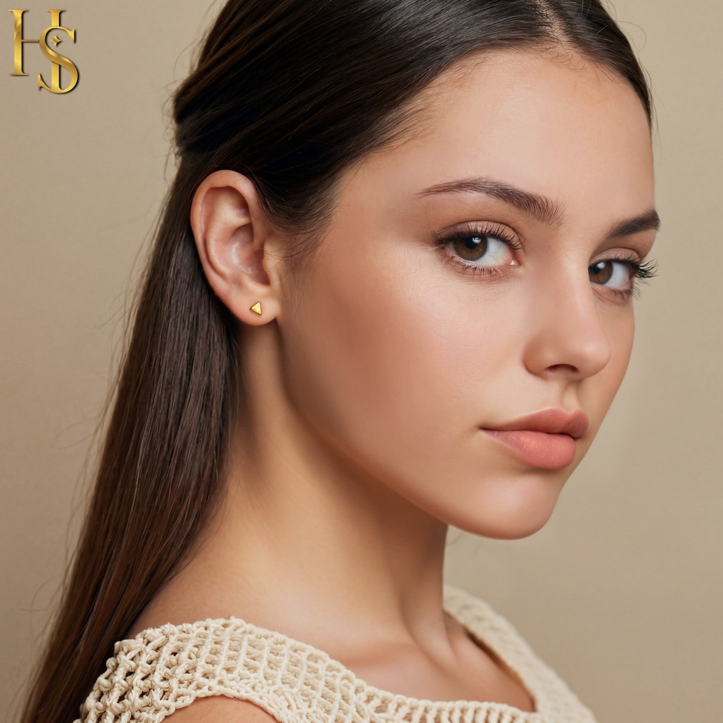 A pair of small, gold-plated triangle stud earrings worn on the ear of a model against a neutral background.