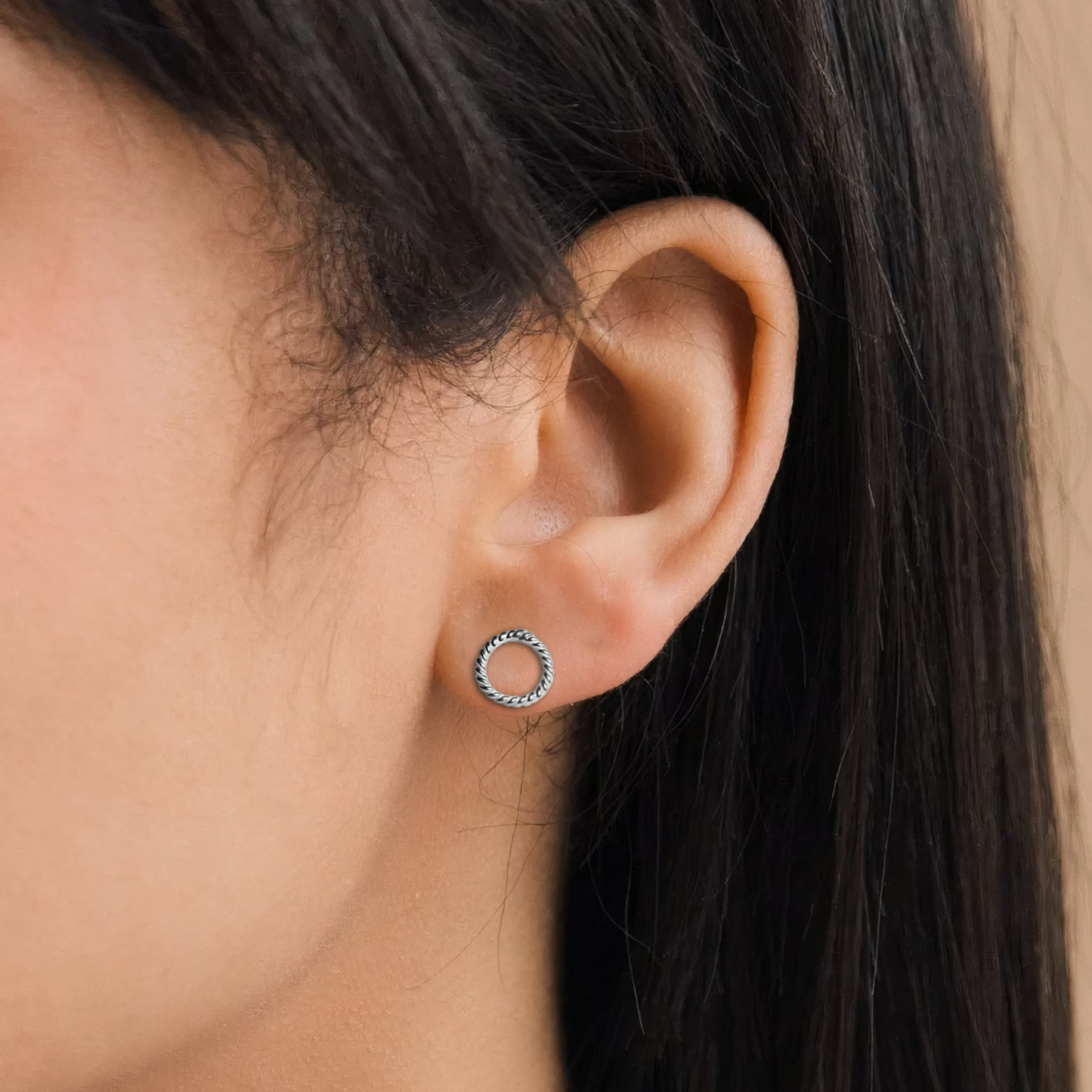 A small, open circle stud earring with a twisted rope design in oxidized sterling silver, worn on the earlobe.