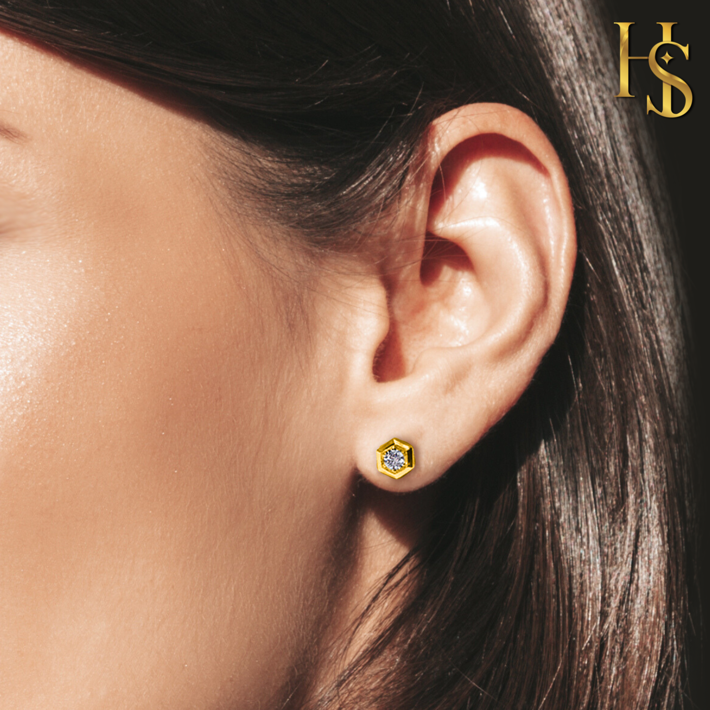 A gold-plated hexagonal stud earring with a round American diamond in a bezel setting, worn on the ear.