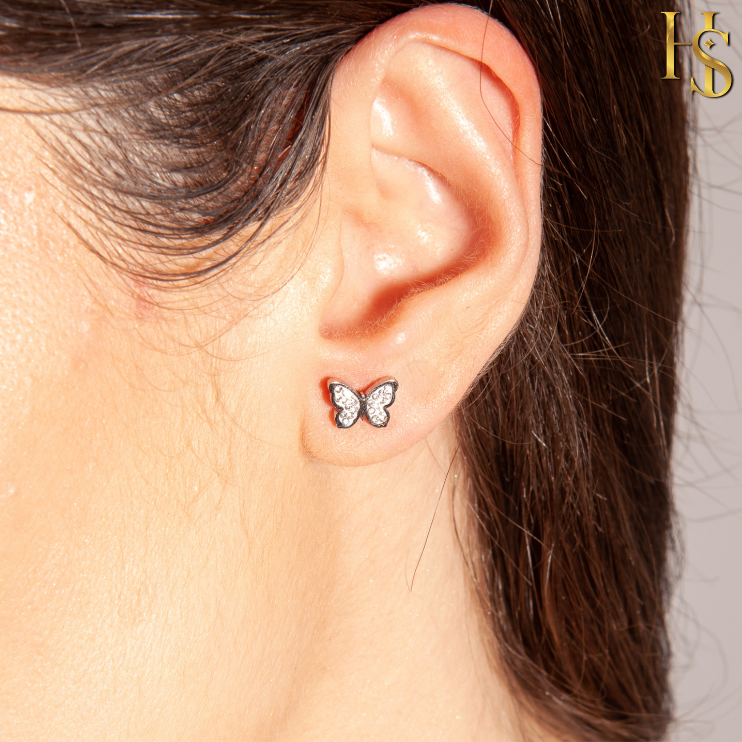 A small butterfly stud earring with pavé-set American diamonds in sterling silver, worn on the earlobe.