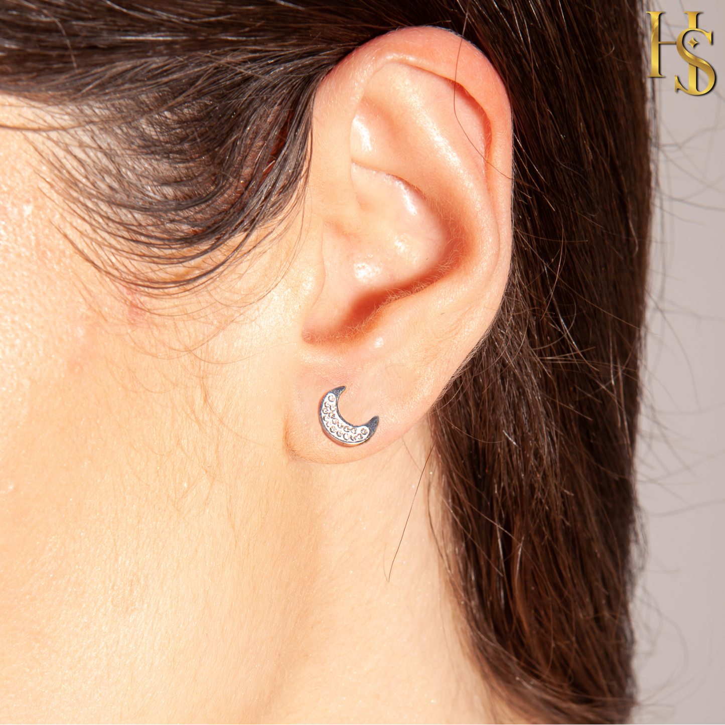 A sterling silver crescent moon stud earring paved with tiny American diamonds, worn on the earlobe.
