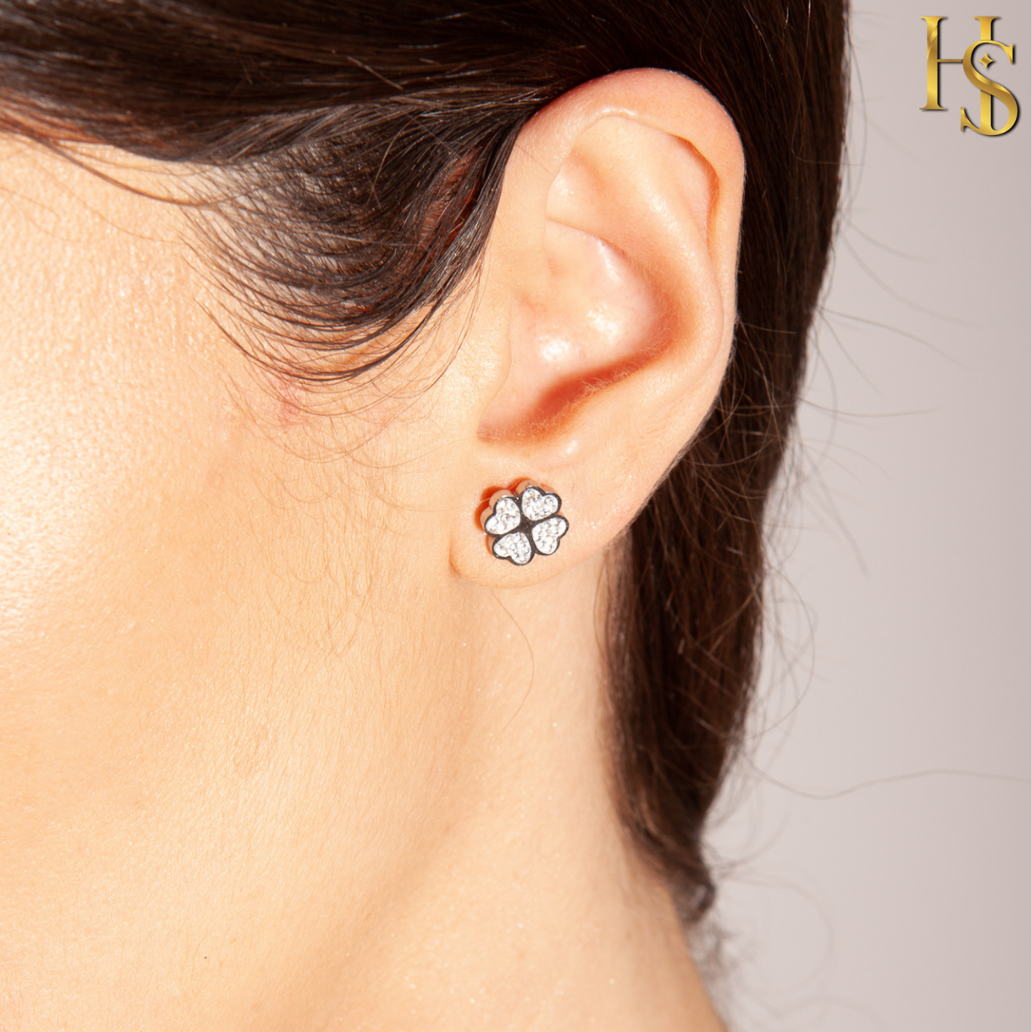 A four-leaf clover stud earring with pavé-set American diamonds in sterling silver, worn on the ear.