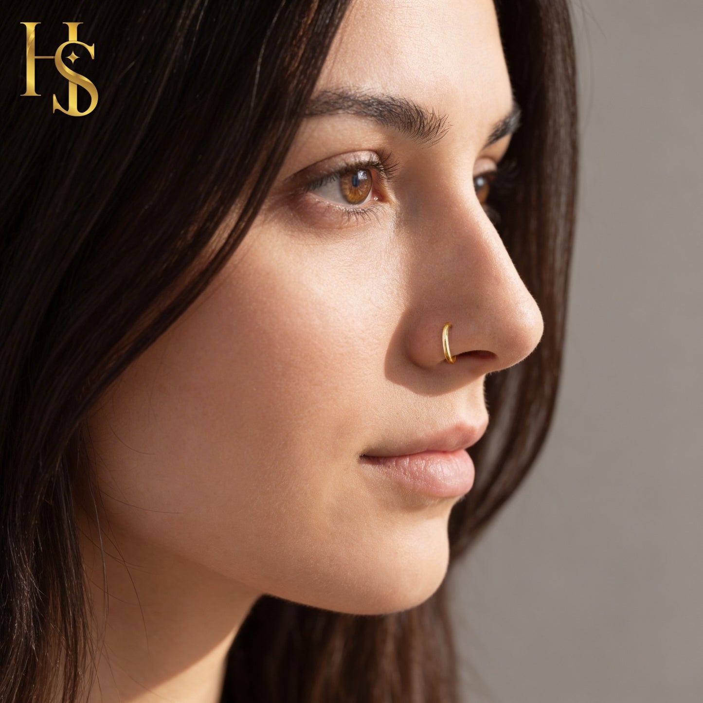 A minimal gold-plated sterling silver nose ring worn on the nostril of a model in a profile view.