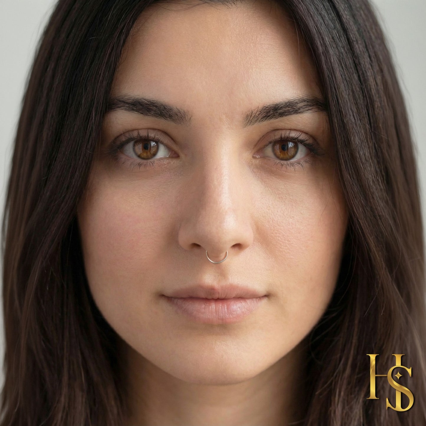 A simple sterling silver septum nose ring with a tiny ball closure is worn by a model with dark hair and brown eyes.