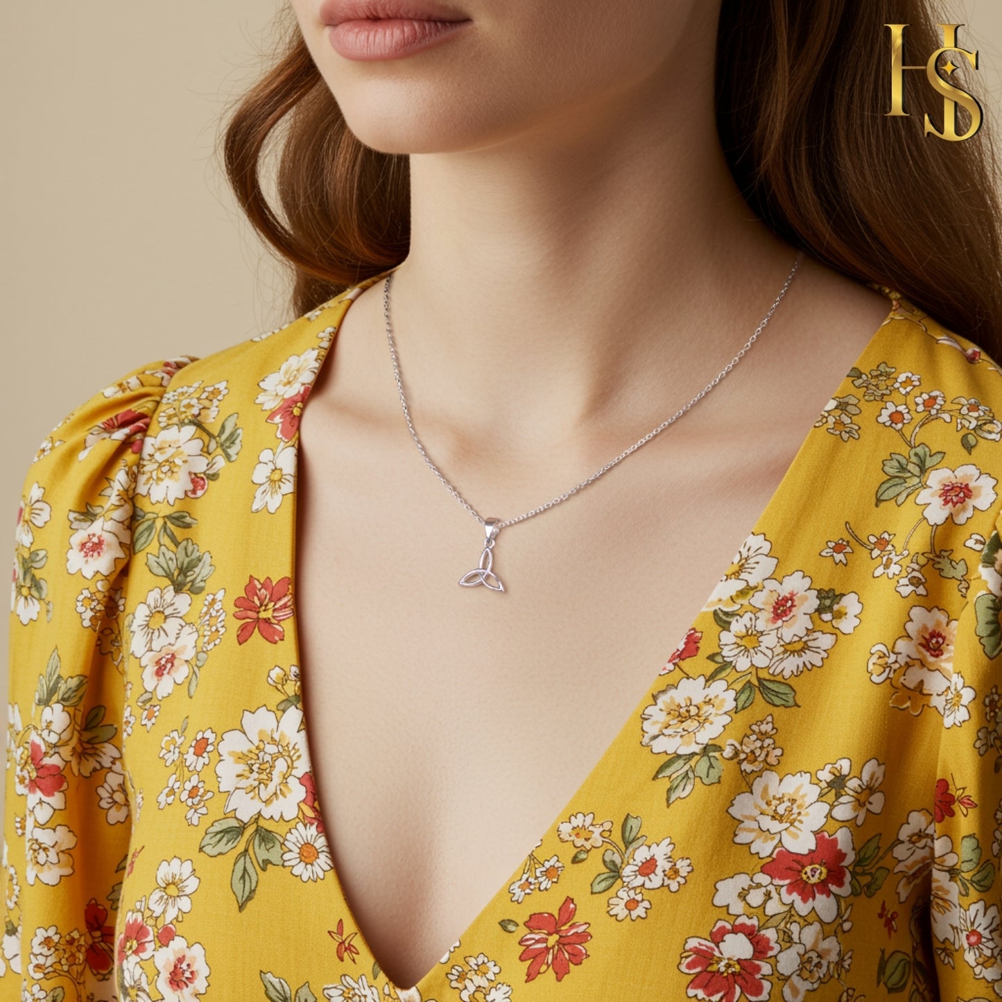 A sterling silver pendant necklace with a Celtic knot design is worn on the neck with a yellow floral dress.