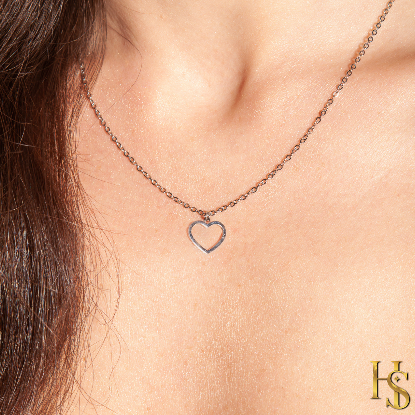 A sterling silver pendant necklace with a small, open heart charm is worn on a model's neck.