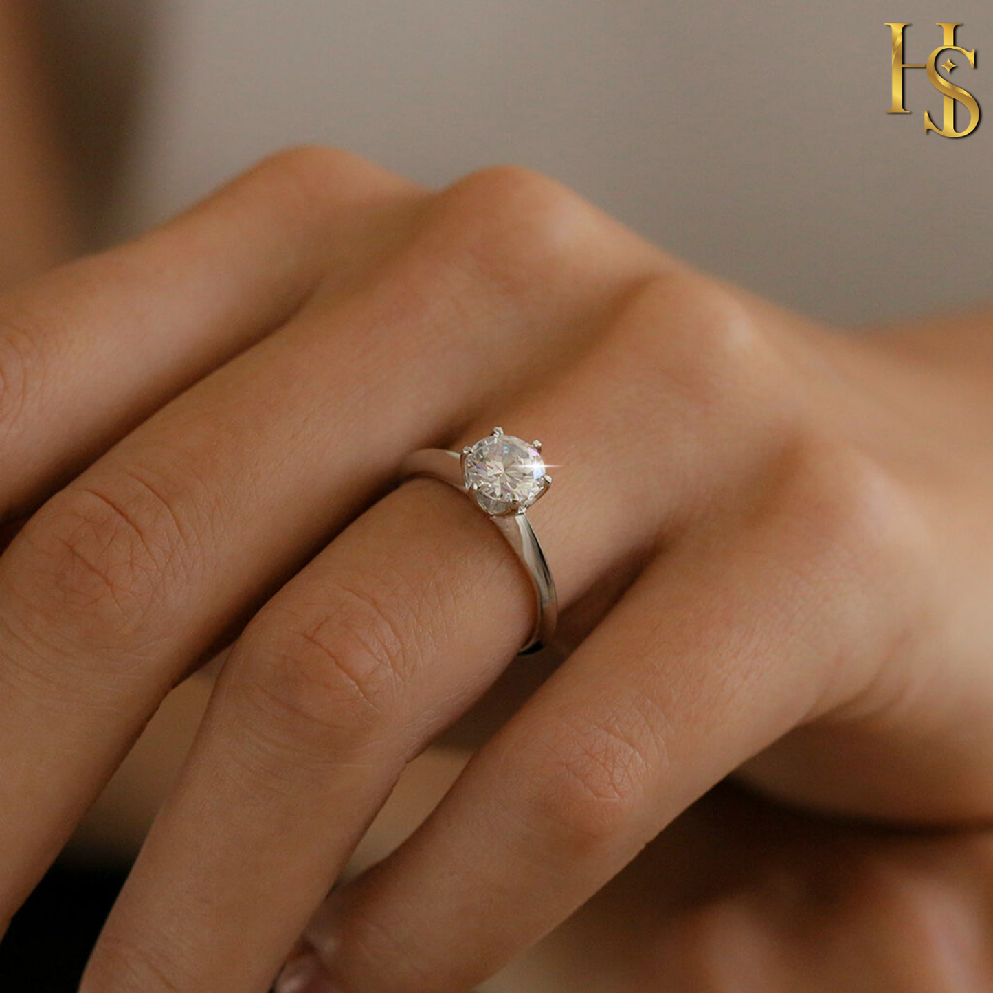 A solitaire ring with a round American diamond in a six-prong setting on a sterling silver band, worn on a woman's finger.