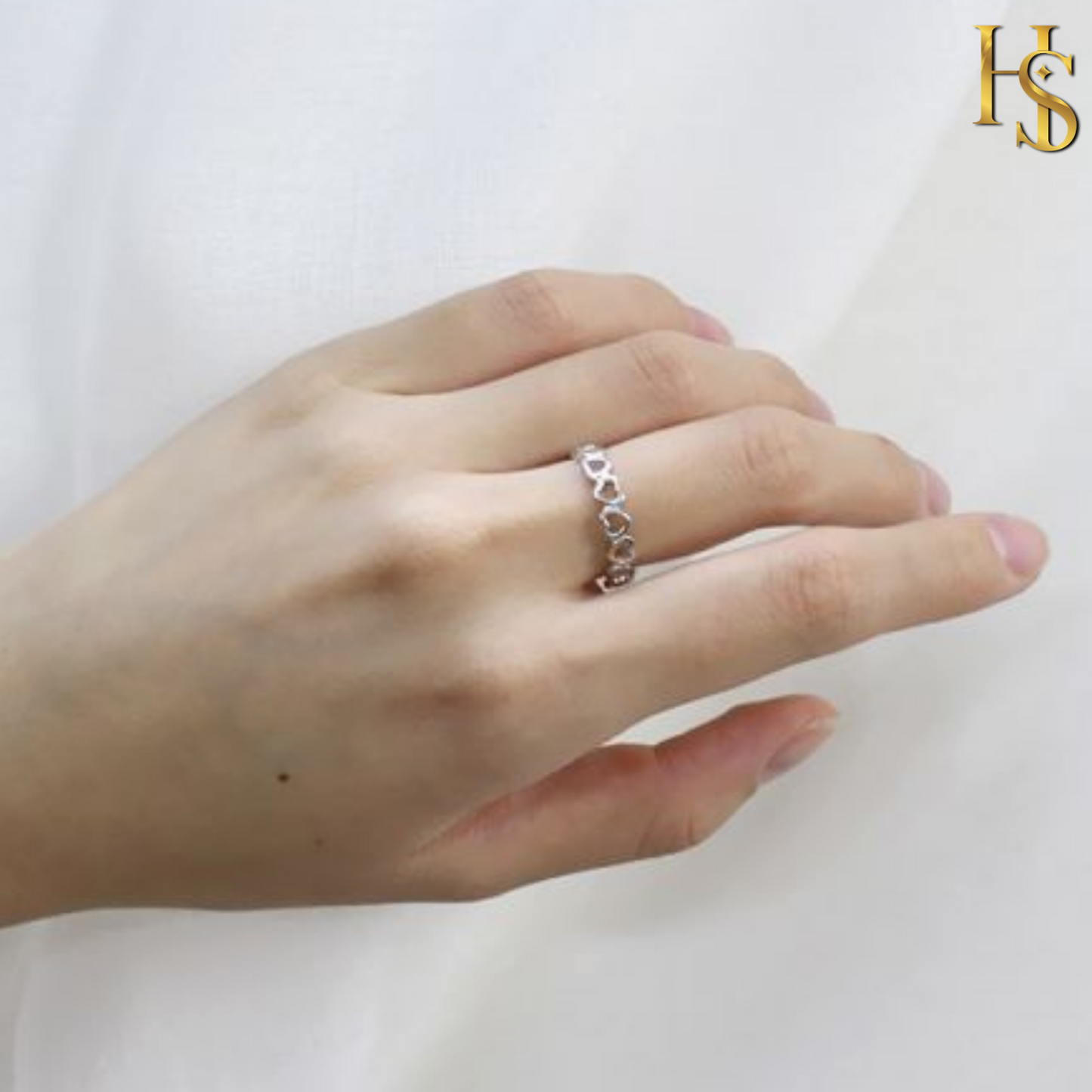 An adjustable sterling silver ring with a cutout heart motif band is worn on a model's hand against a soft white fabric background.