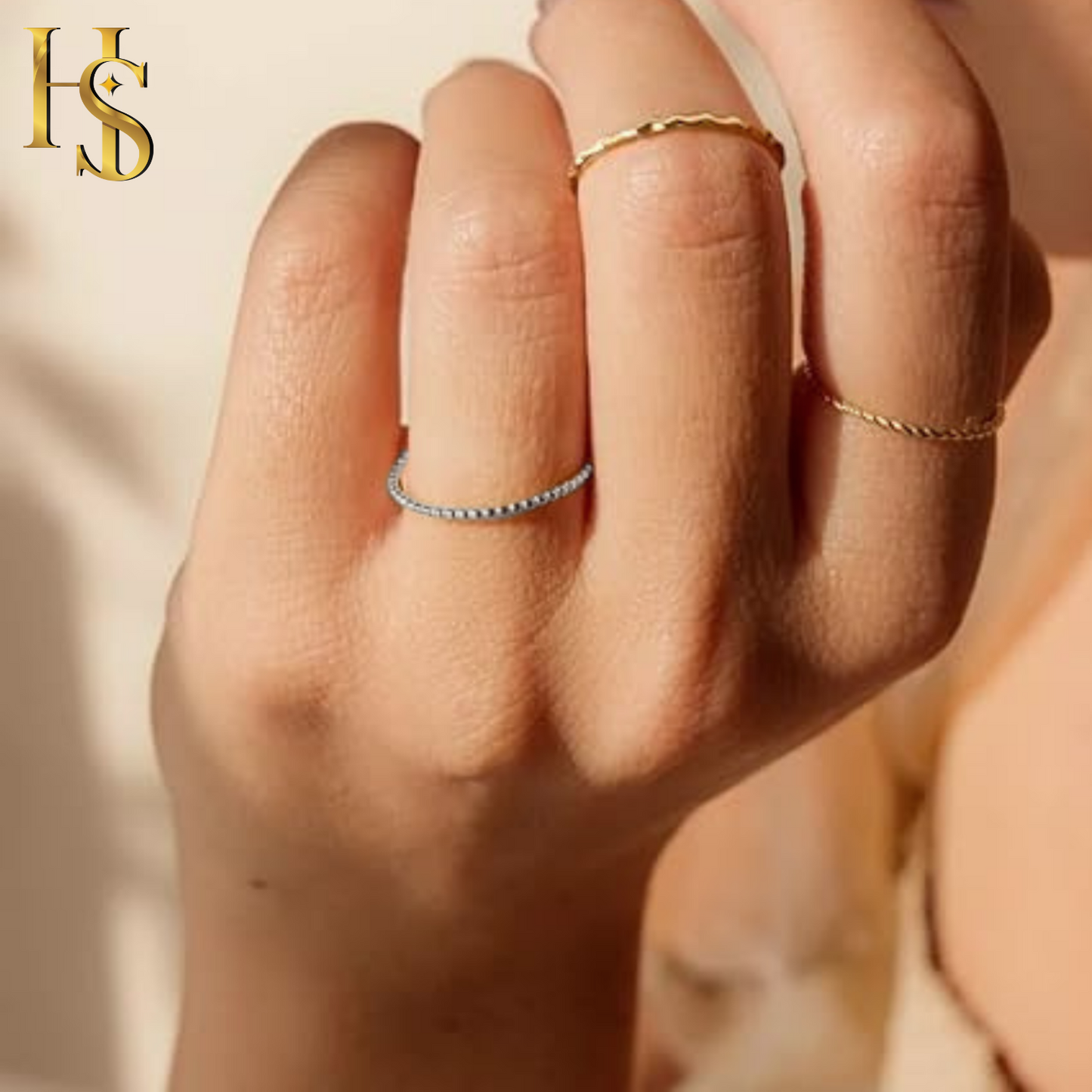 A dainty beaded sterling silver ring worn on a finger, stacked with other gold-plated rings in soft, warm light.
