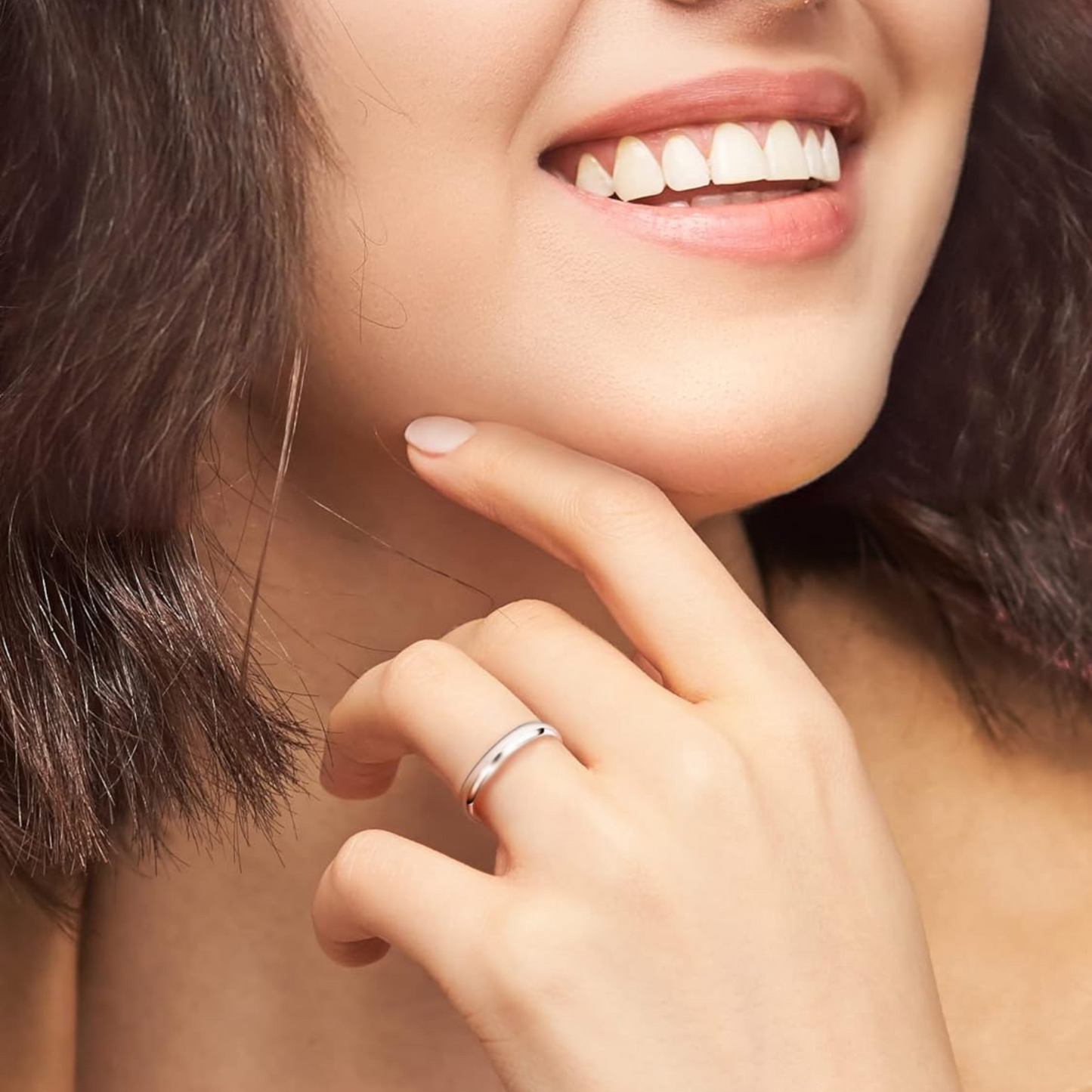 A classic sterling silver band ring with a smooth, polished finish worn on a woman's hand as she smiles.