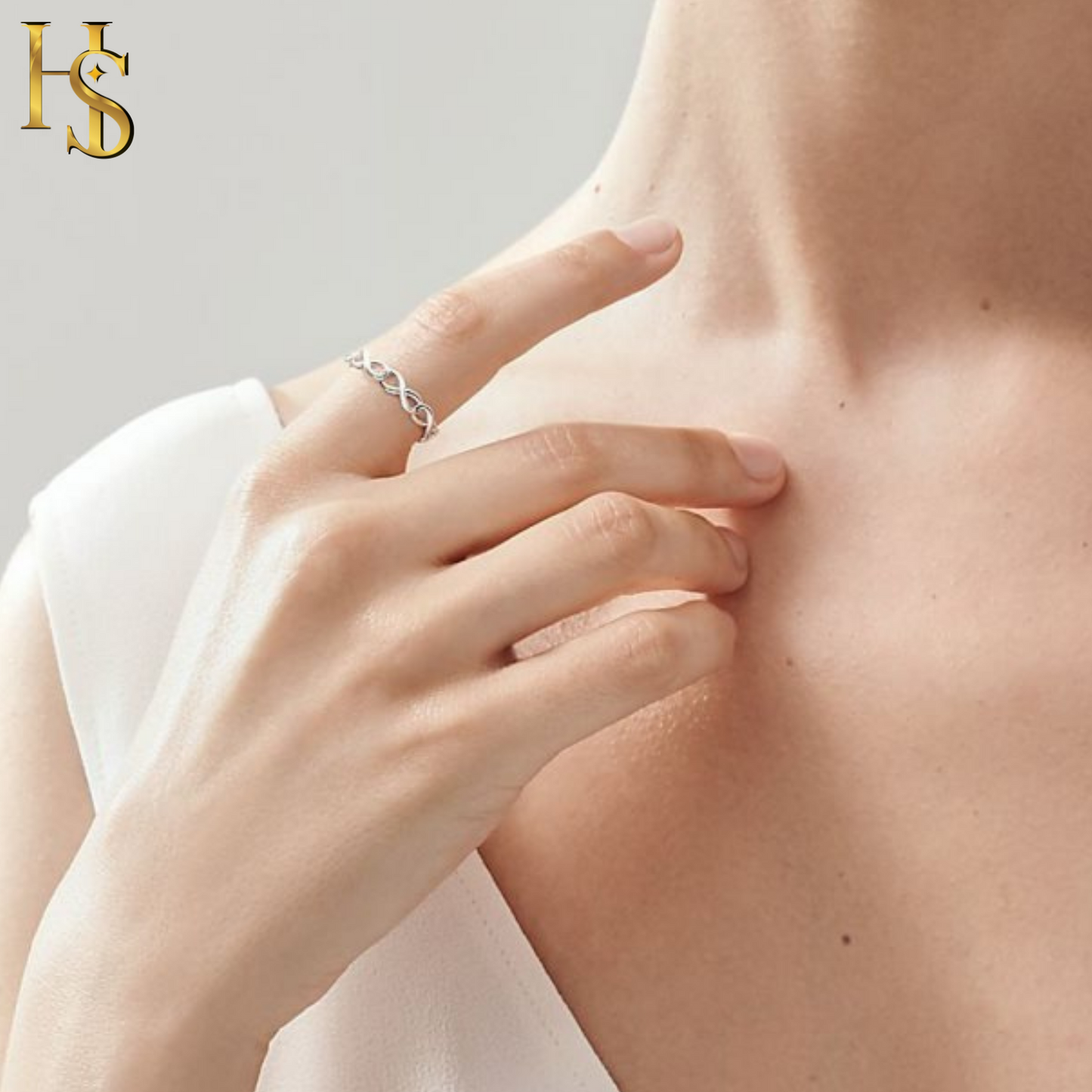 A sterling silver band ring with a continuous infinity symbol design worn on a model's finger, with her hand resting near her neck.