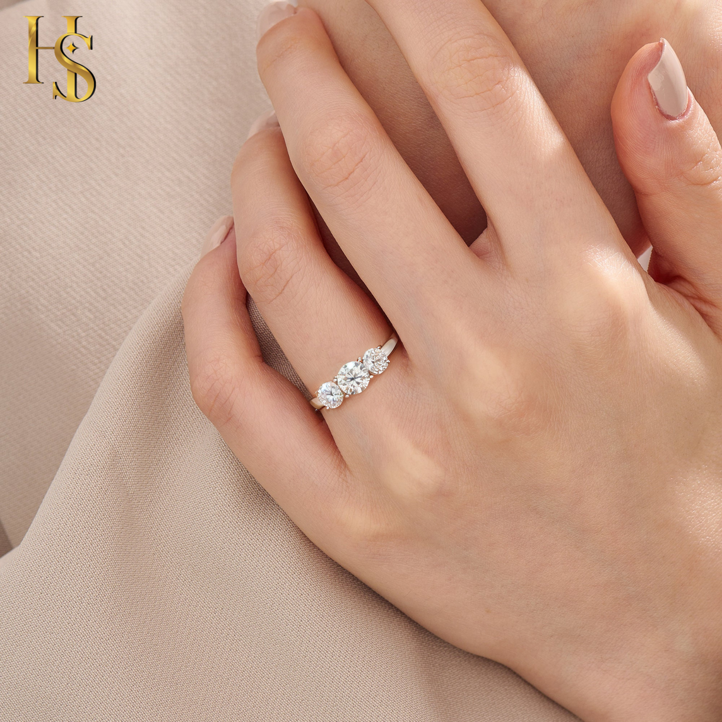 A sterling silver adjustable ring with three round American diamonds in a prong setting worn on the finger against a beige fabric.