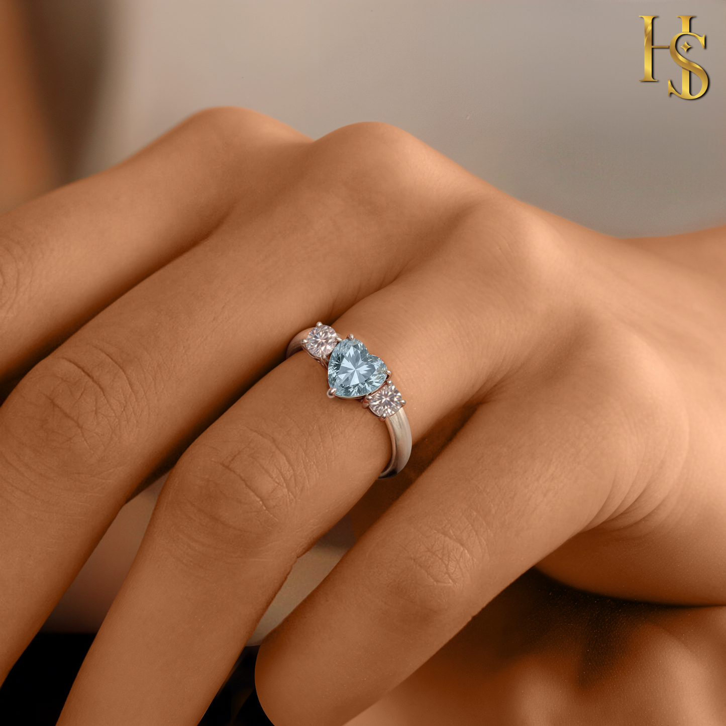 A sterling silver three-stone ring with a heart-shaped blue stone and two round American diamonds worn on a woman's hand.