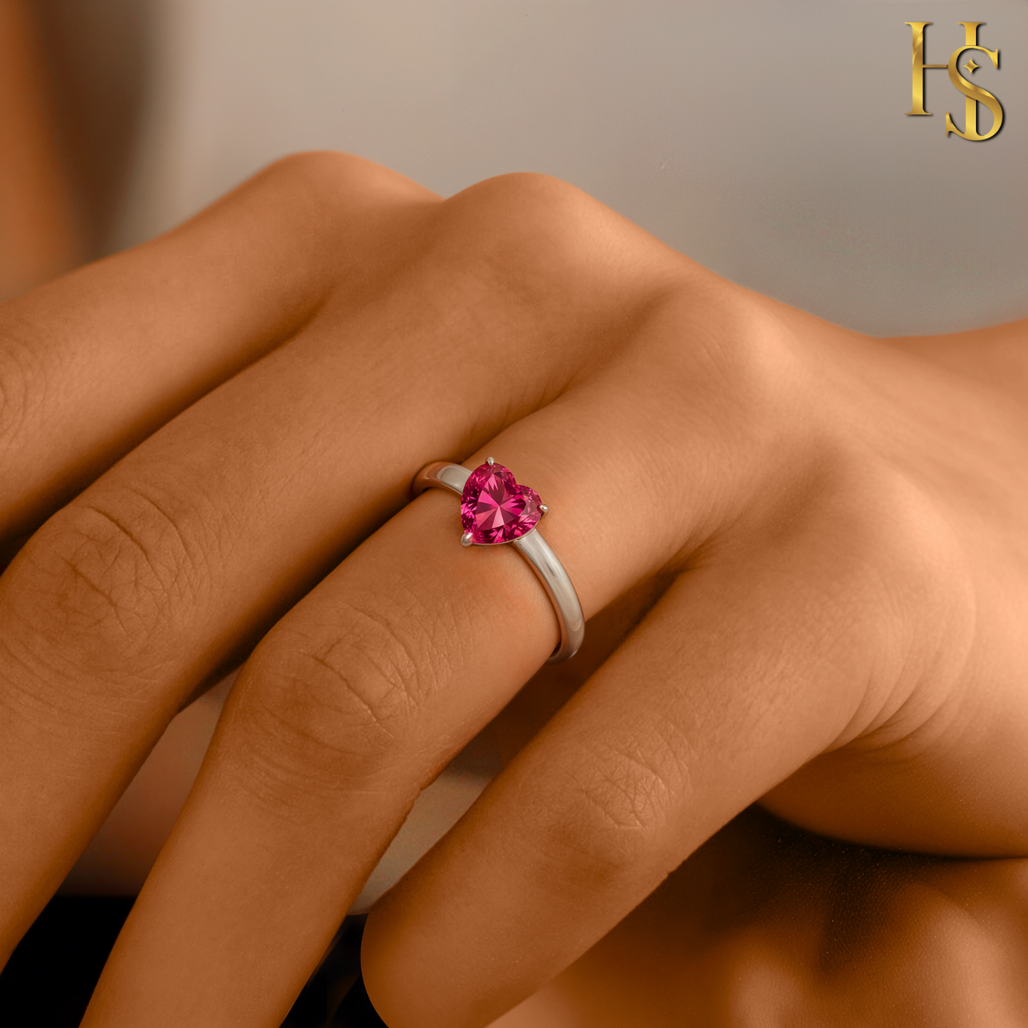 A solitaire ring with a heart-shaped pink stone in a prong setting on a sterling silver band, worn on a woman's finger.
