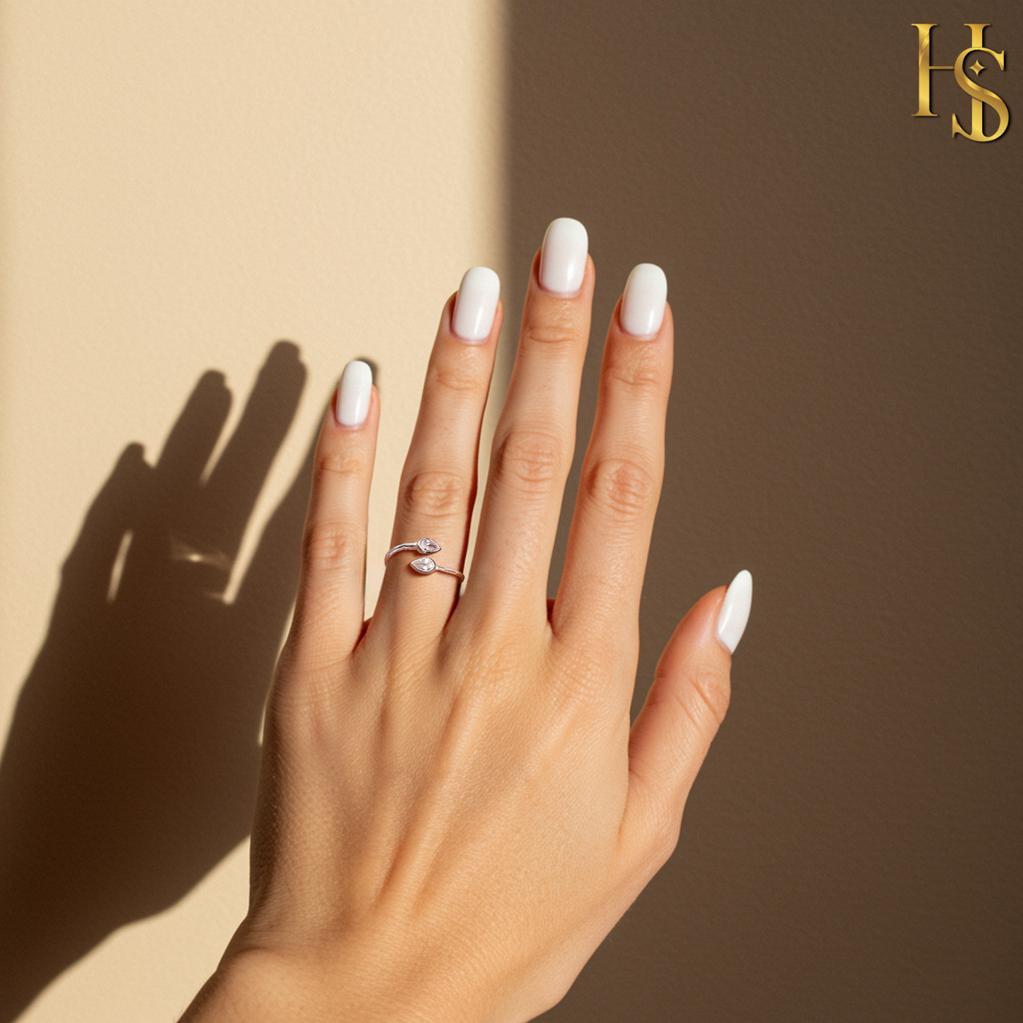 An adjustable sterling silver ring with two marquise-cut American diamonds in a bezel setting worn on a hand against a beige background.