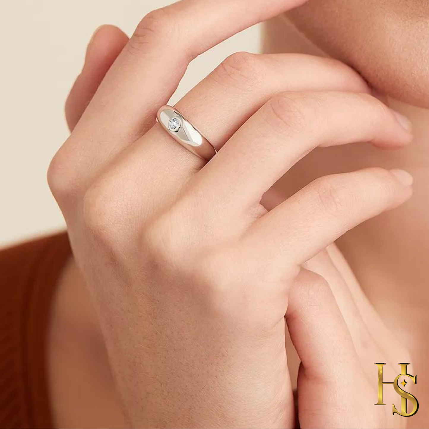 A sterling silver band ring with a single round American diamond in a bezel setting is worn on the finger.