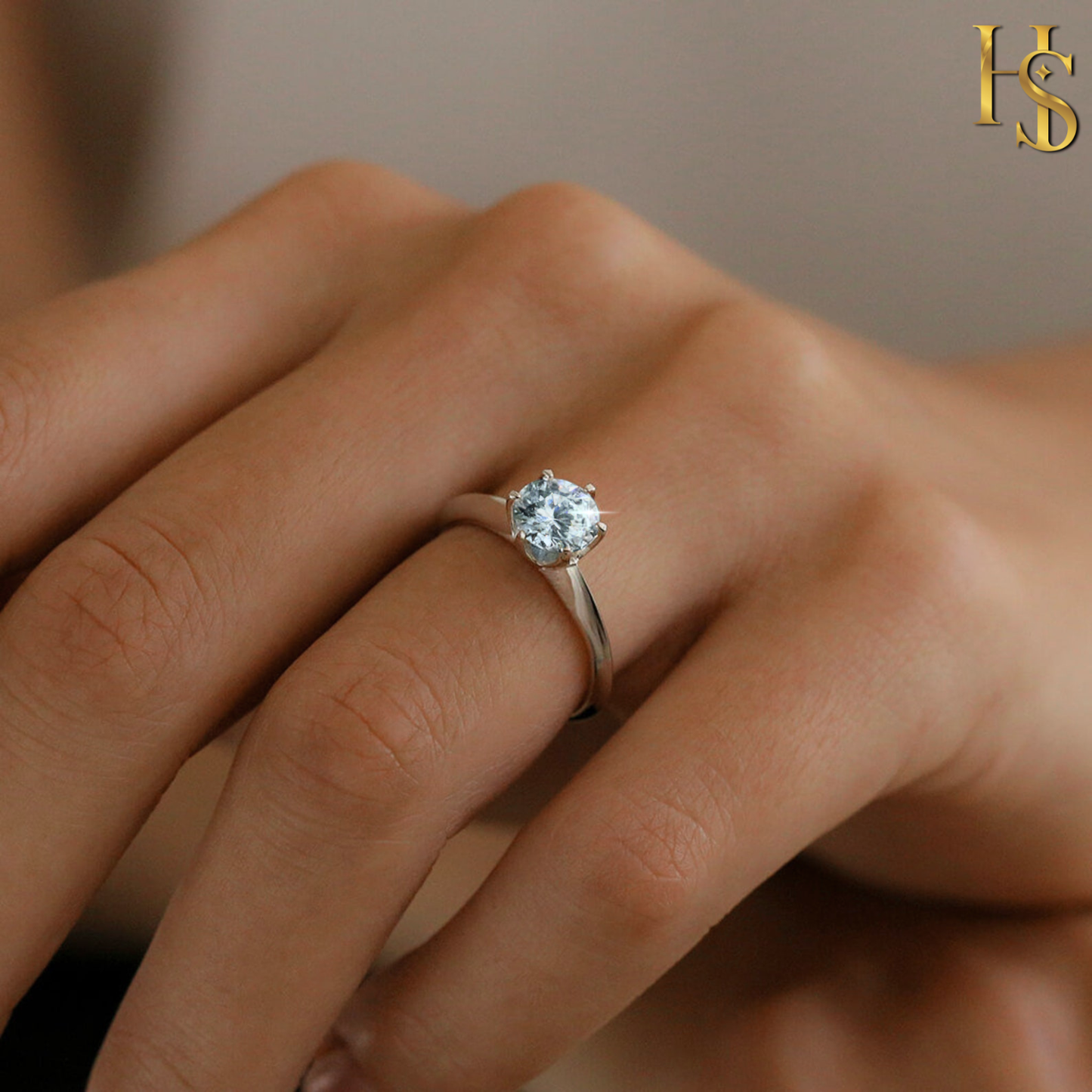 A solitaire ring with a round aquamarine American diamond in a six-prong setting on a sterling silver band, worn on a model's hand.