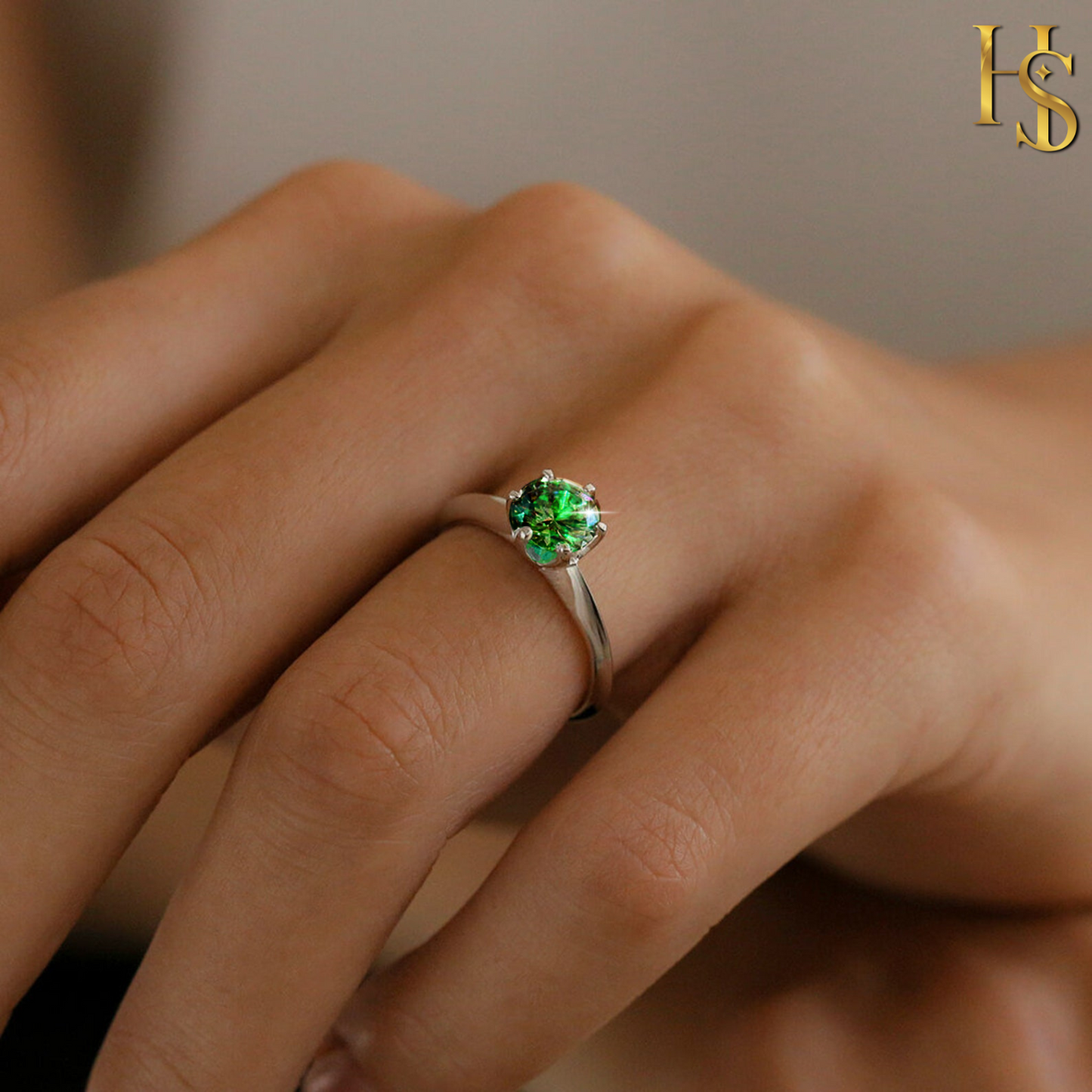 A sterling silver solitaire ring with a round, brilliant-cut emerald green stone in a six-prong setting, worn on a person's hand.