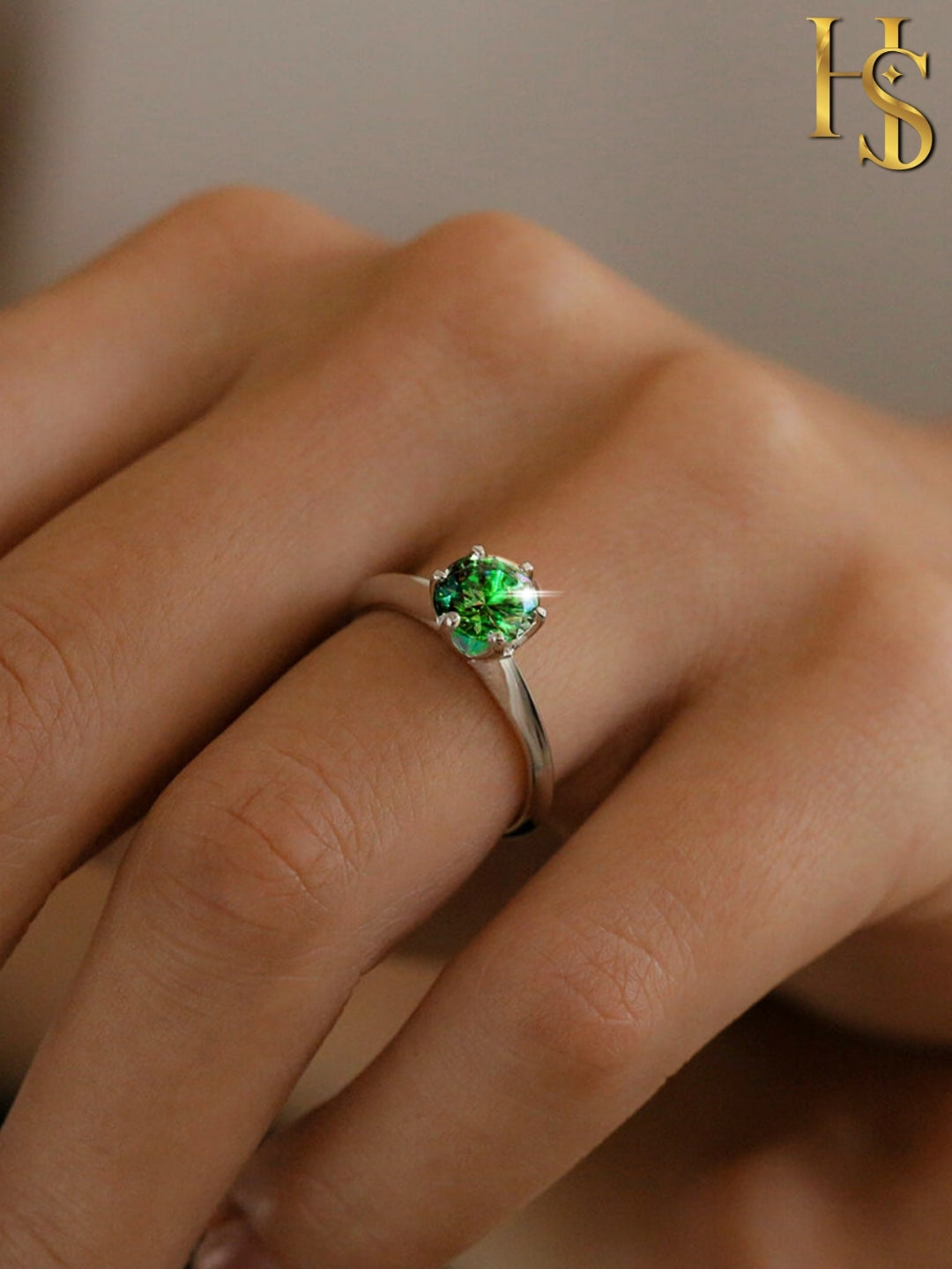 A solitaire ring with a round emerald green stone in a six-prong setting on a sterling silver band, worn on a person's finger.