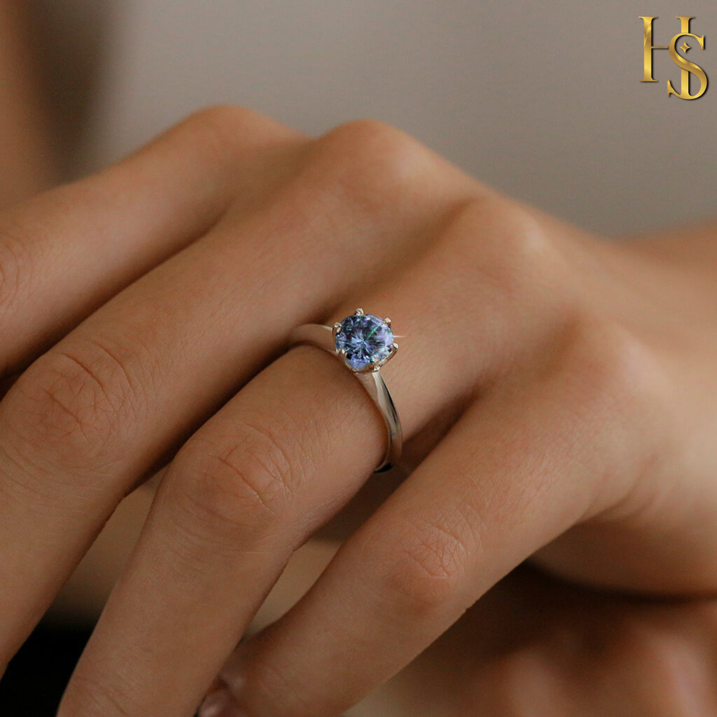 A solitaire ring with a round-cut sapphire American diamond in a six-prong setting on a sterling silver band, worn on a finger.