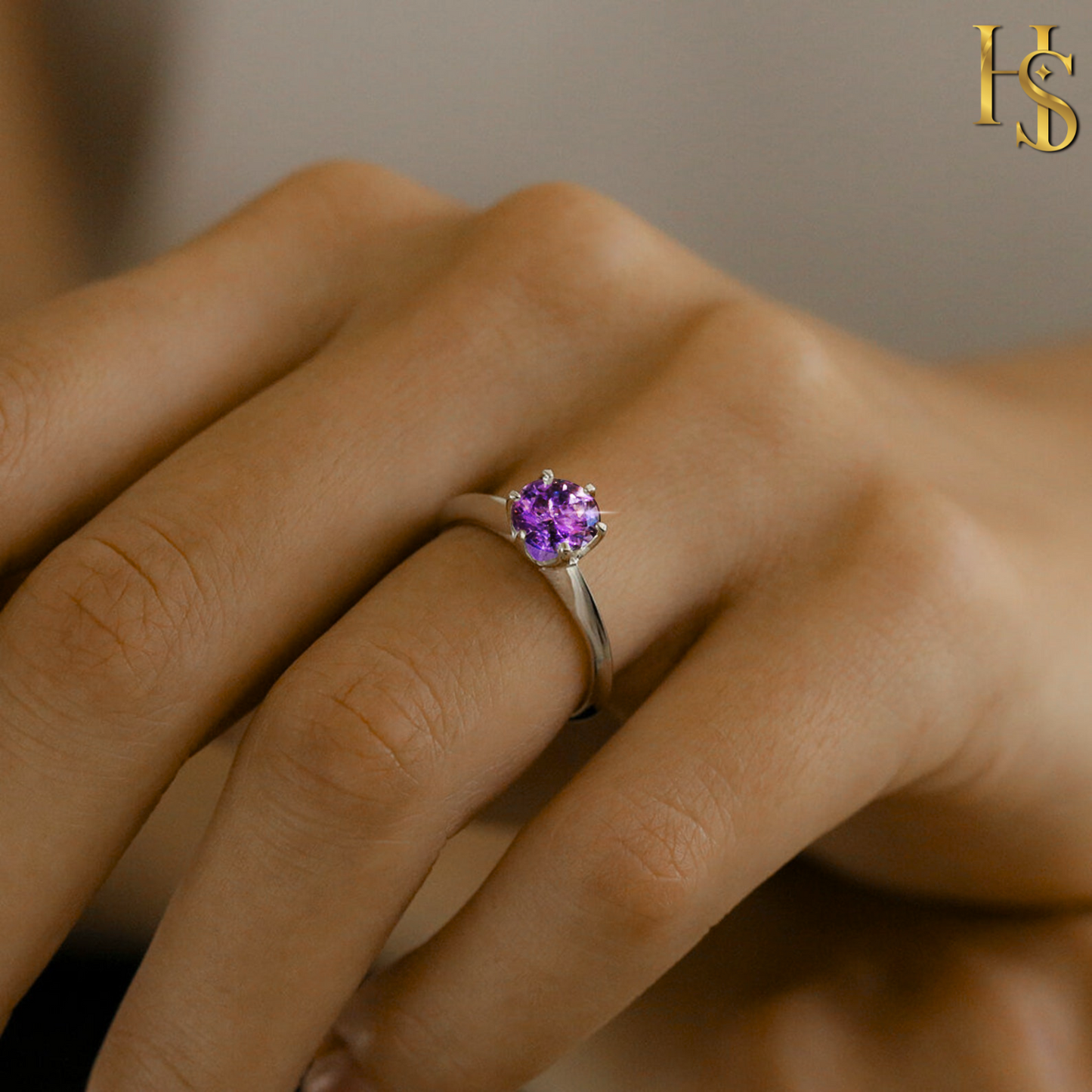 A solitaire ring with a round-cut purple amethyst in a six-prong setting on a sterling silver band, worn on a model's finger.