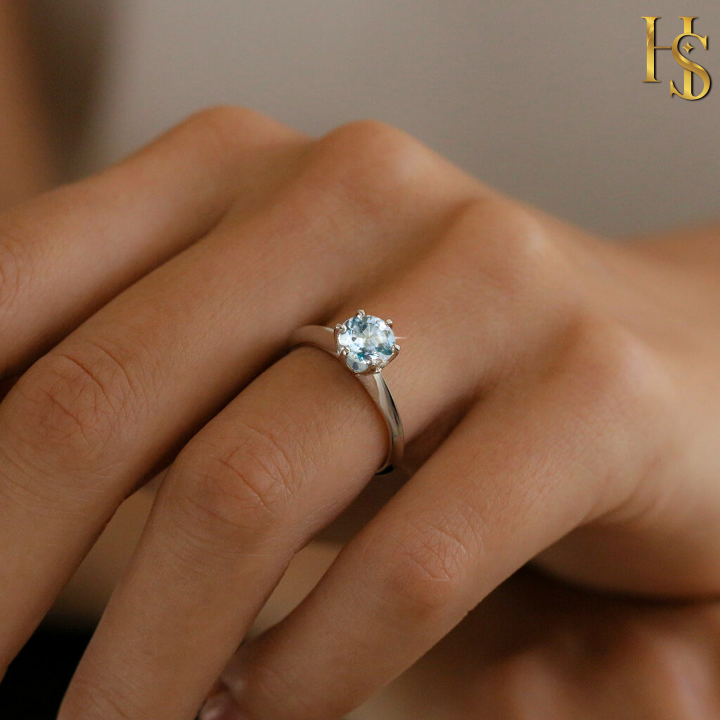 A sterling silver solitaire ring with a round blue topaz gemstone in a six-prong setting, worn on a person's finger.