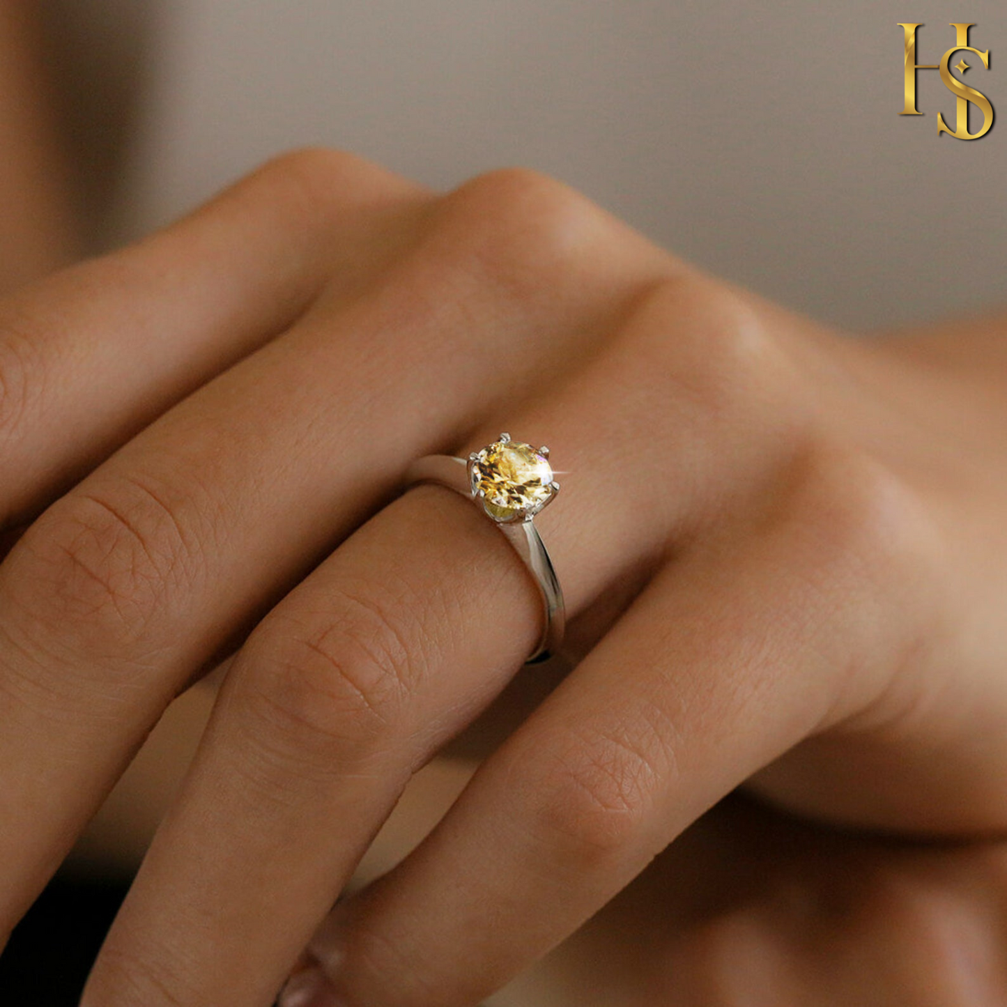 A solitaire ring with a round-cut yellow citrine gemstone in a six-prong setting on a sterling silver band, worn on a model's hand.
