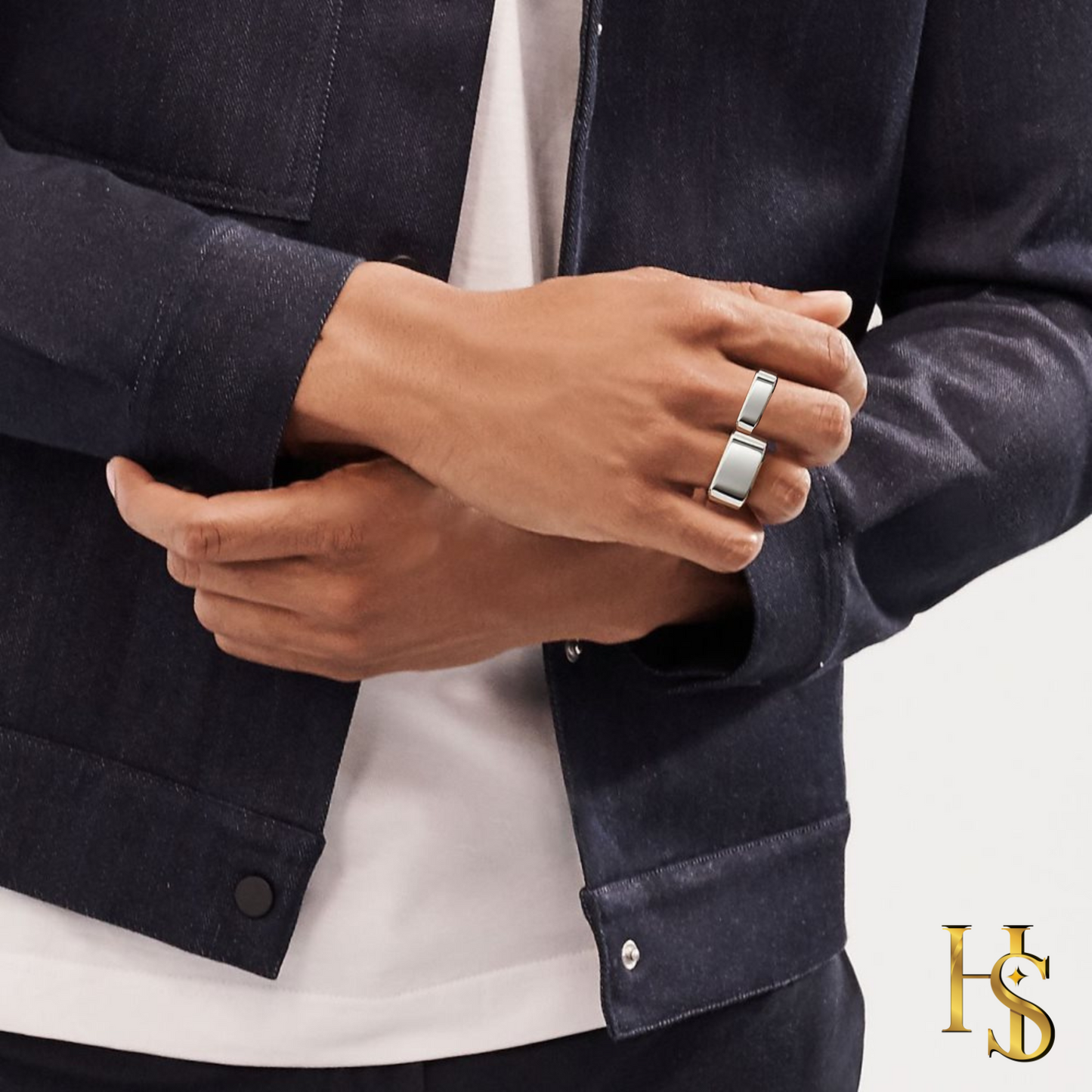 A pair of sterling silver signet band rings with a flat rectangular top worn on a man's hand against a dark denim jacket.