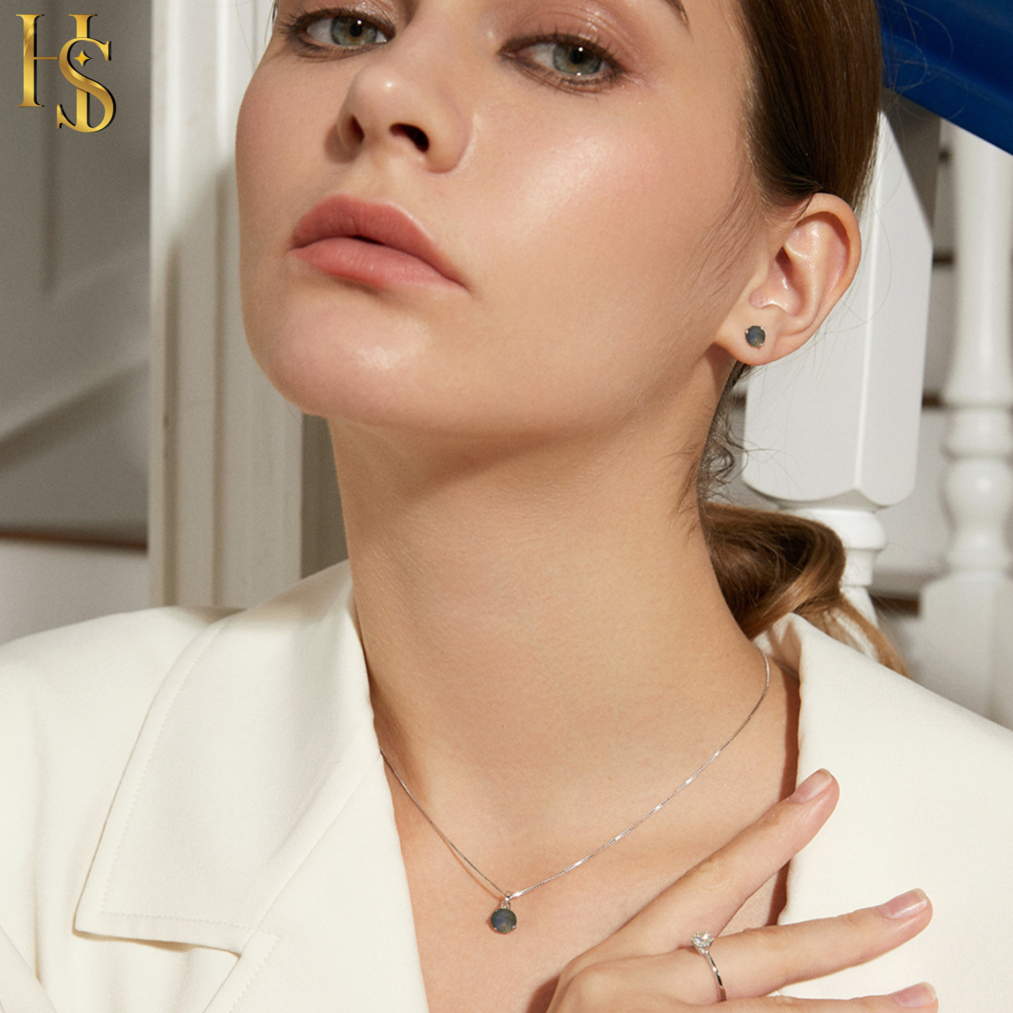 A woman wears a sterling silver pendant set with a round labradorite gemstone on a box chain and matching stud earrings.