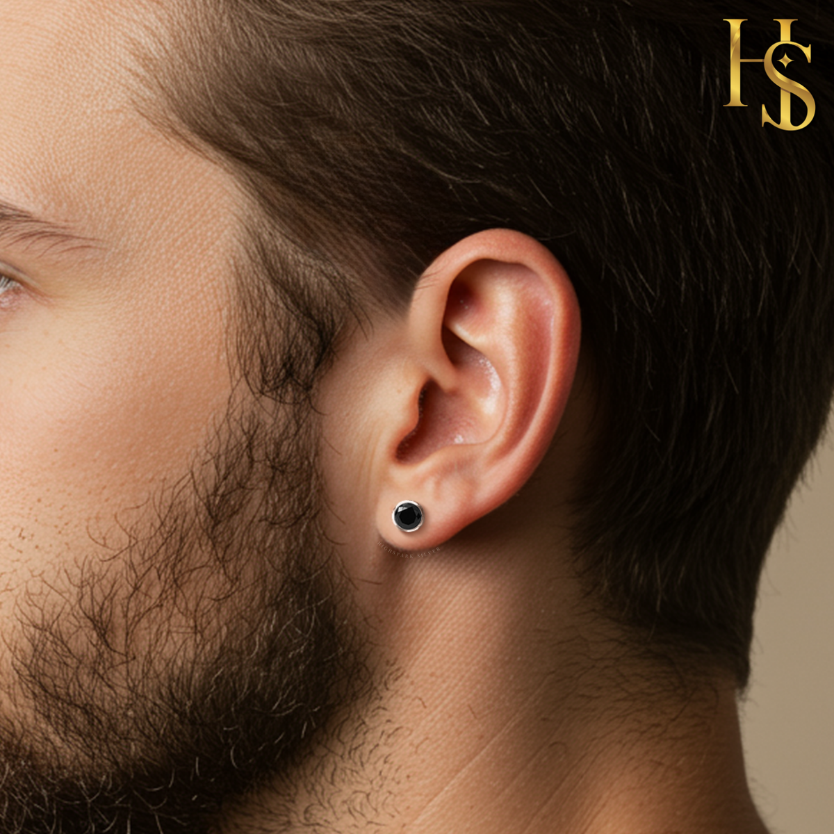 A round black solitaire stud earring in a sterling silver bezel setting, worn on a man's earlobe.