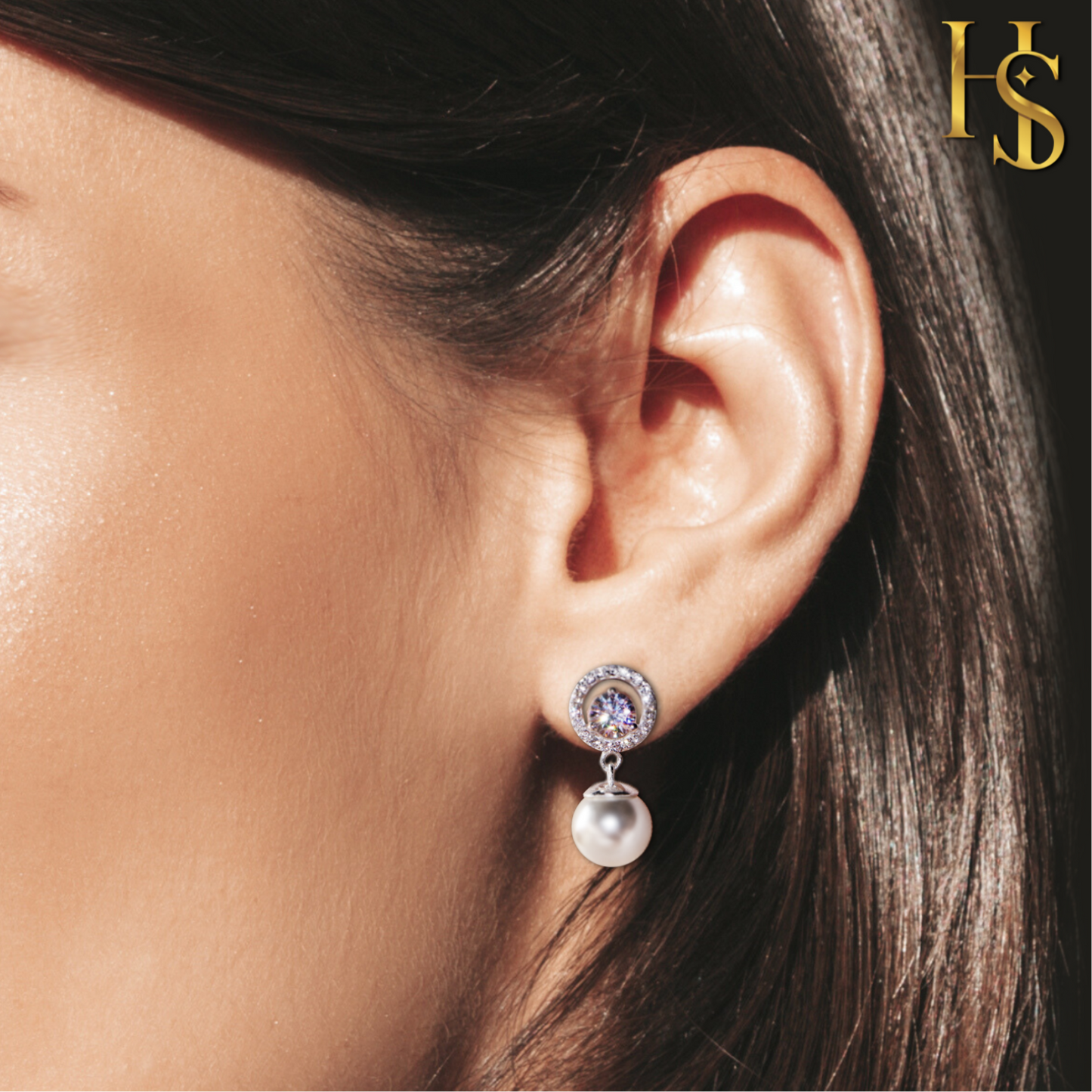 Sterling silver drop earrings with a central American diamond in a halo setting and a dangling pearl, worn on the ear.