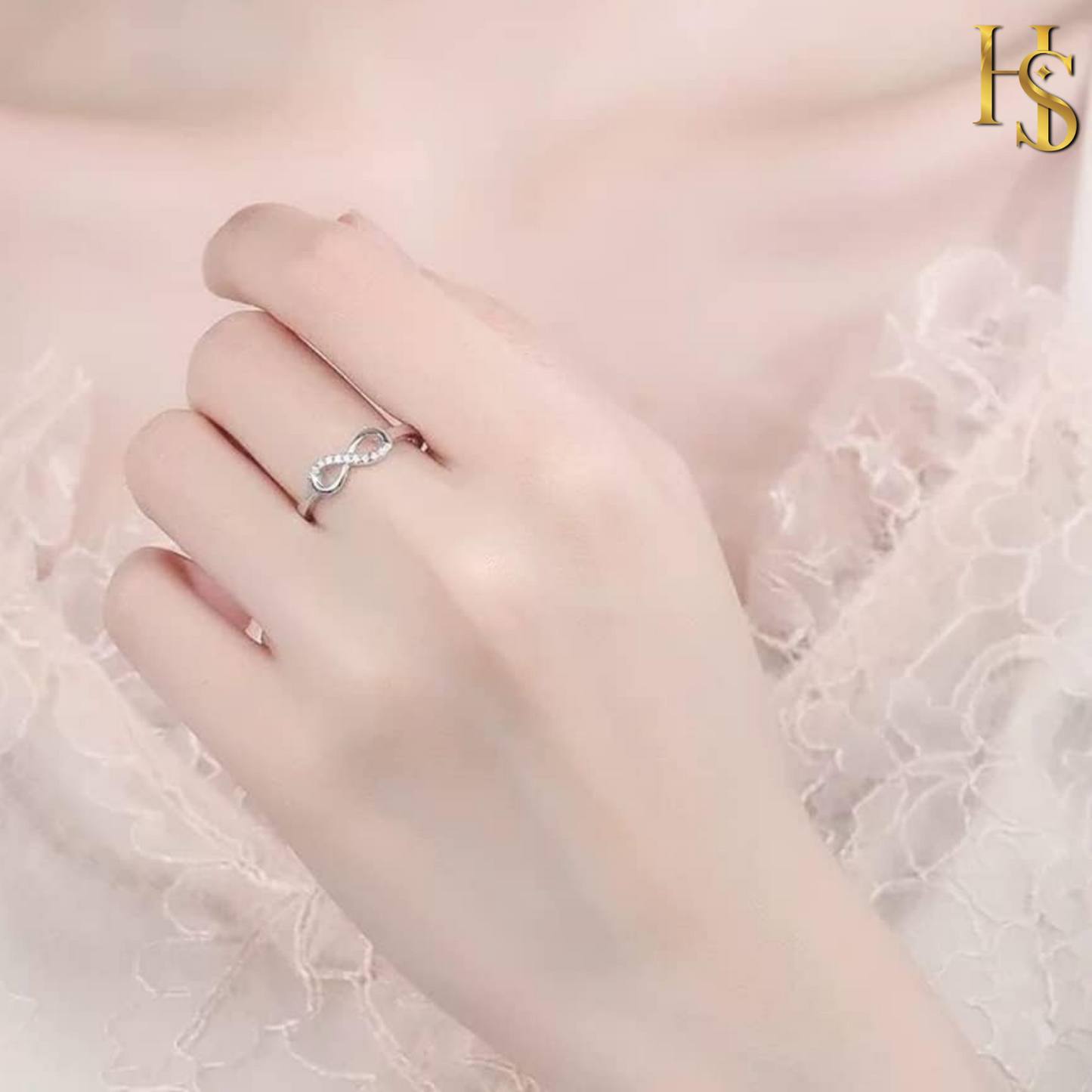 A sterling silver infinity ring, partially paved with American diamonds, worn on the finger against a delicate white lace background.