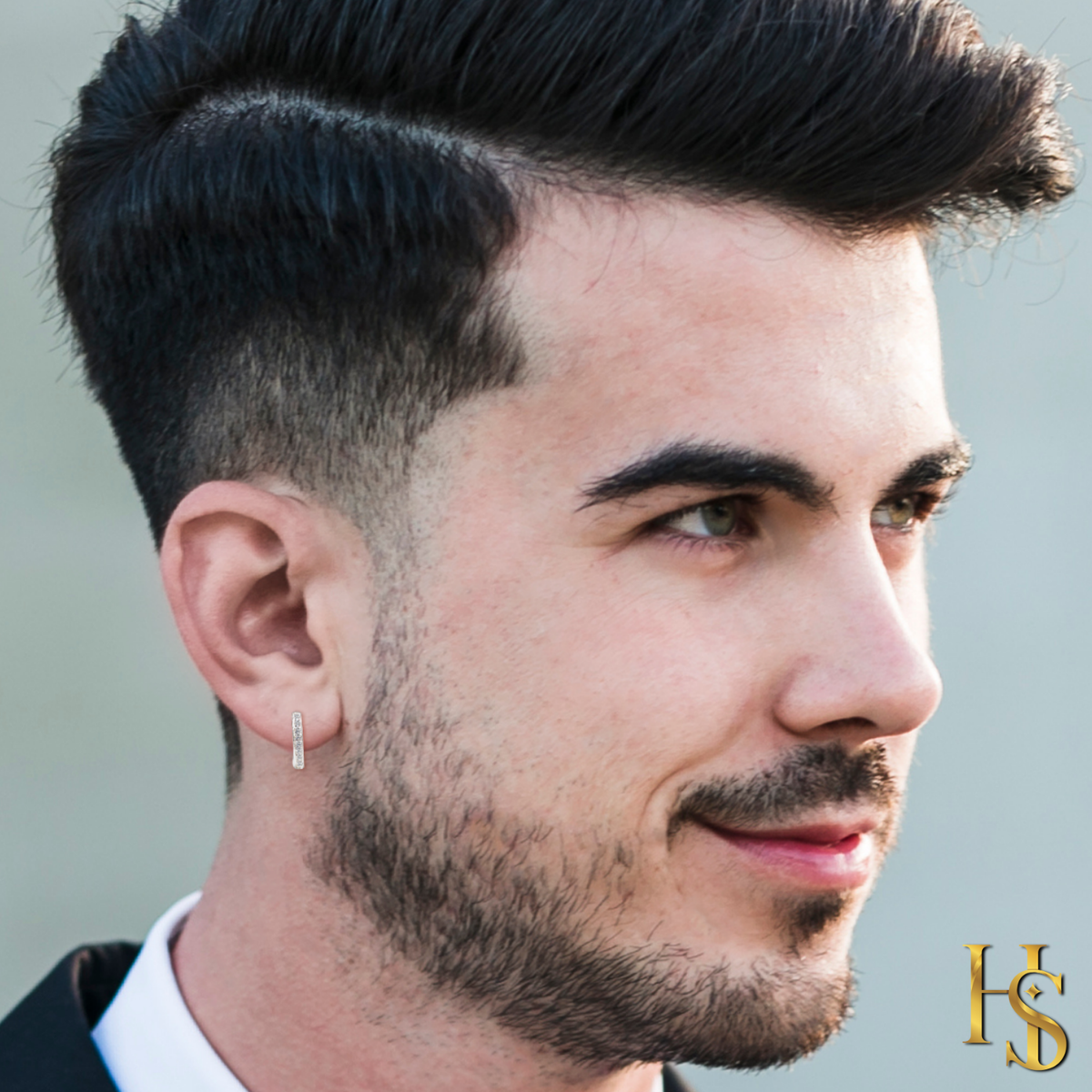 A sterling silver half hoop earring for men, channel-set with a row of tiny American diamonds, worn on the ear of a model.