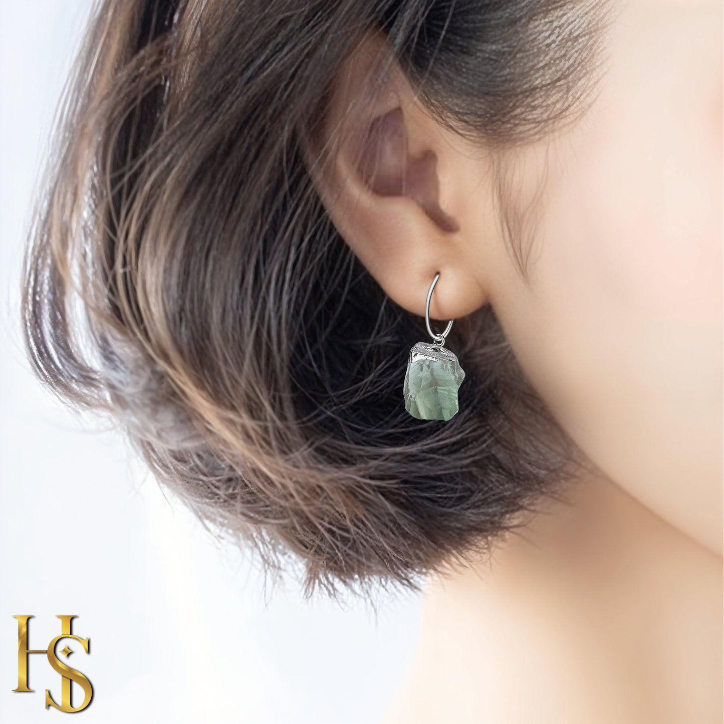 A sterling silver hoop earring with a dangling raw-cut green amethyst gemstone worn on the ear.