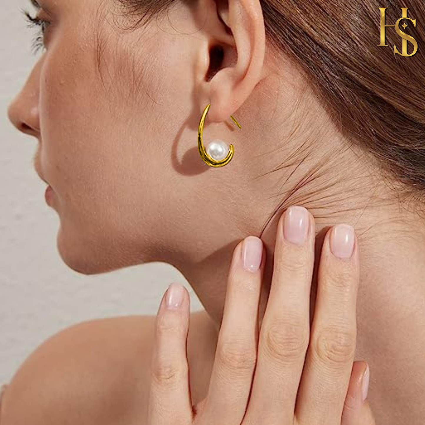 A gold-plated J-hoop earring with a single nested pearl worn on a model's ear, with her hand gently touching her neck.