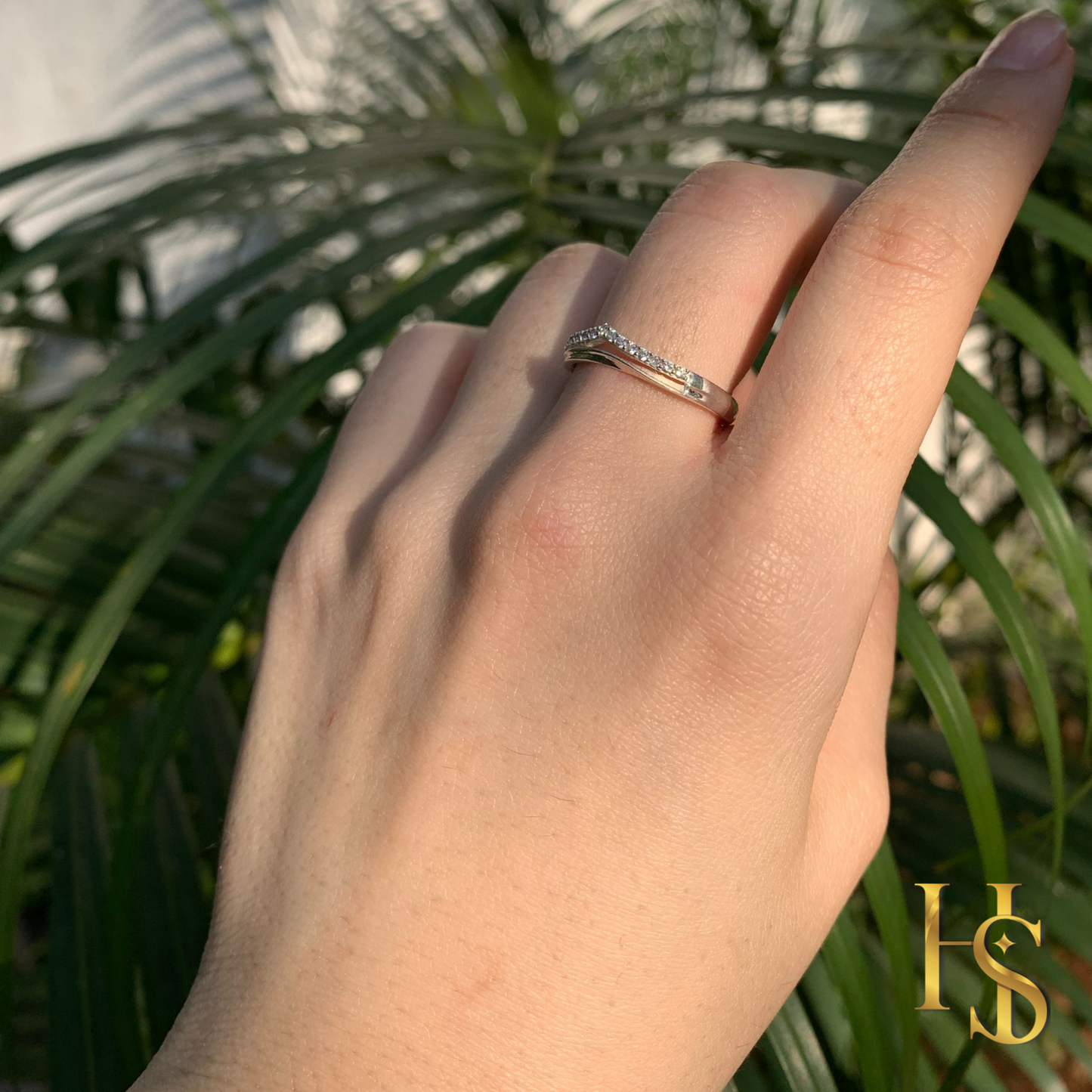 A sterling silver crown ring with pavé-set American diamonds worn on a hand in front of green palm leaves.
