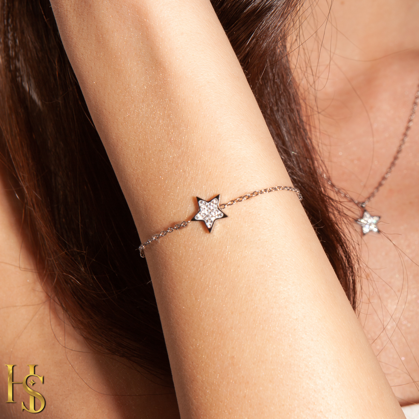 A sterling silver chain bracelet with a star charm paved with American diamonds, worn on a model's wrist.