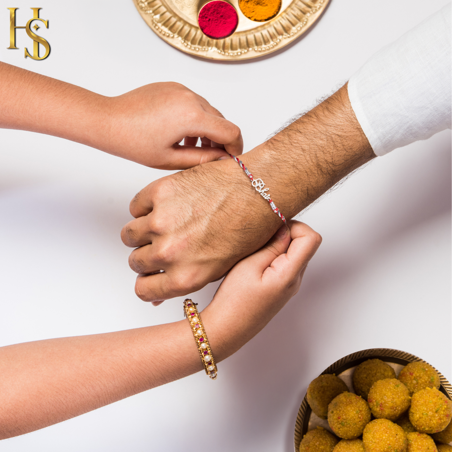 A sister ties a 925 sterling silver rakhi with a 'Bhai' motif onto her brother's wrist, shown with a pooja thali and sweets.