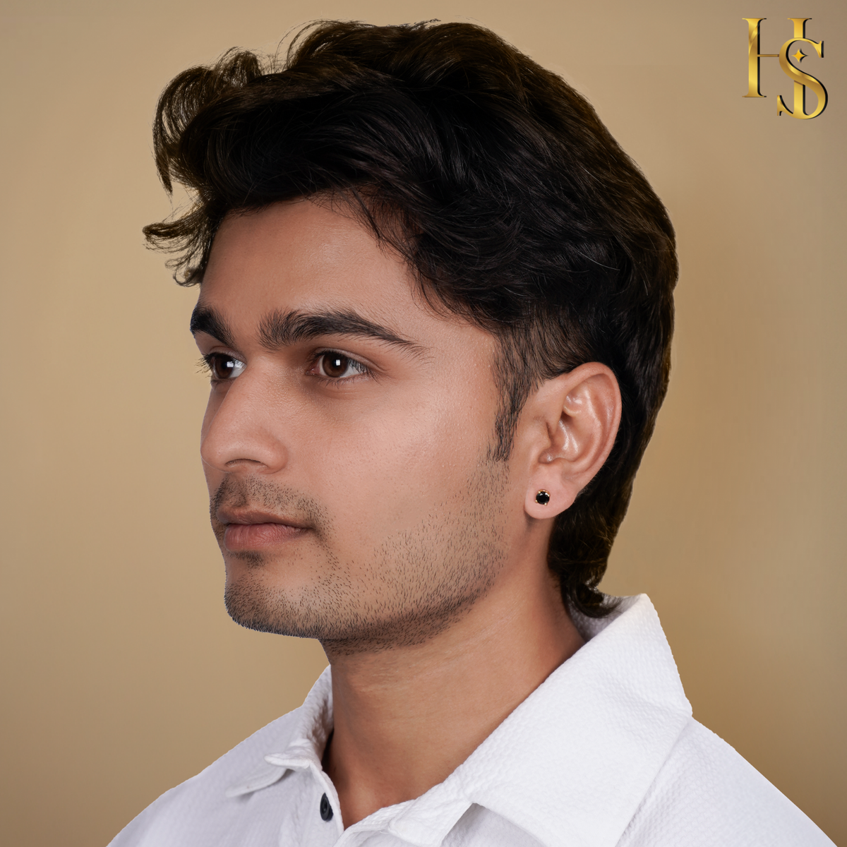 A round black solitaire stud earring in a gold-plated setting worn on a male model's ear against a plain beige background.