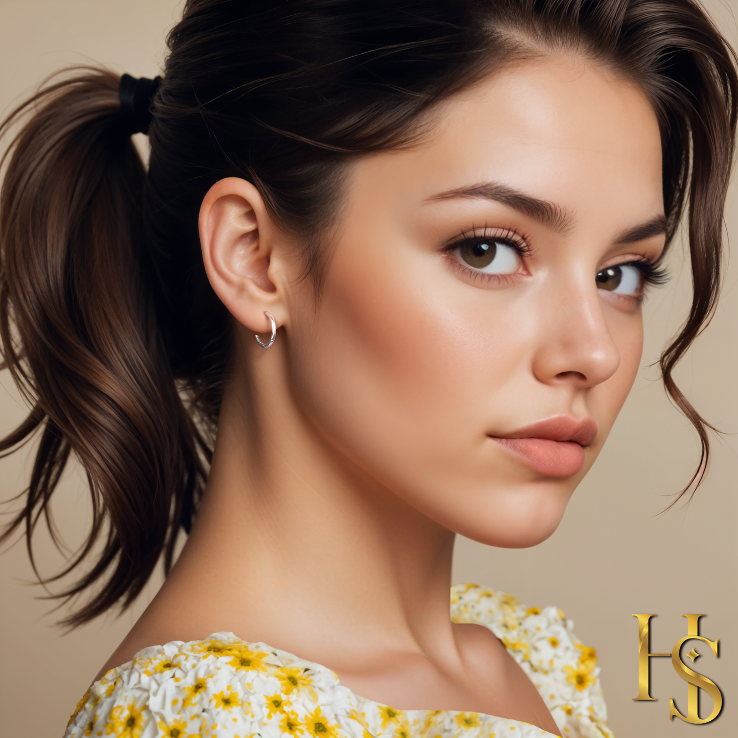 A pair of small, twisted sterling silver hoop earrings worn on the ear of a model with her hair in a ponytail.