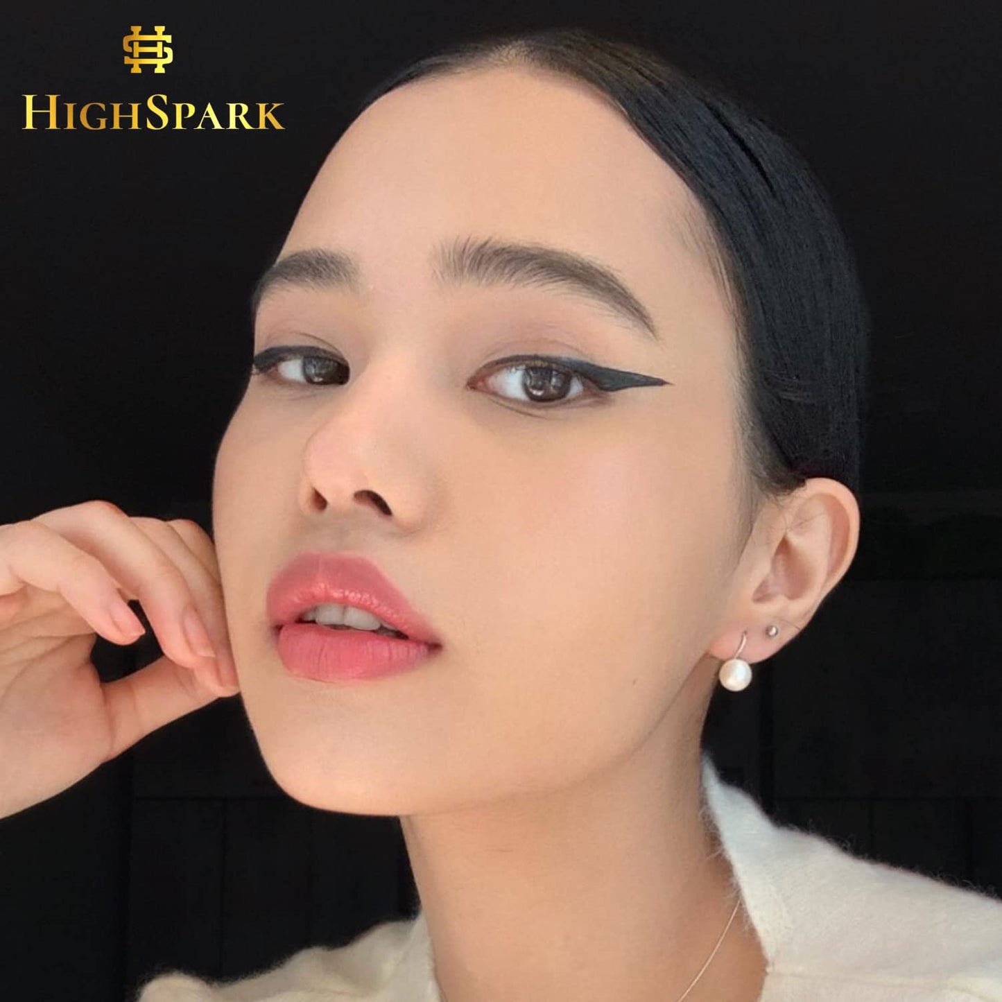 A round white pearl drop earring with a sterling silver hook, worn on the ear by a model with winged eyeliner.