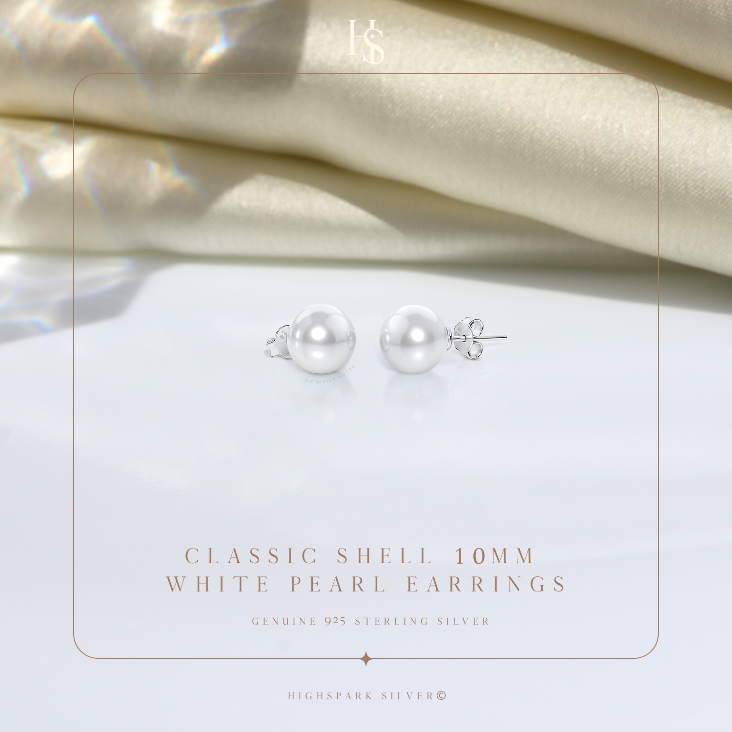 A pair of classic white pearl stud earrings in sterling silver, styled on a white surface with draped cream satin in the background.
