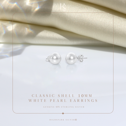 A pair of classic white pearl stud earrings in sterling silver, styled on a white surface with draped cream satin in the background.