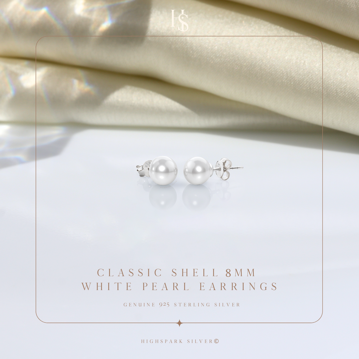 A pair of classic pearl stud earrings in sterling silver with push-back closures, styled on a reflective surface with draped cream satin.