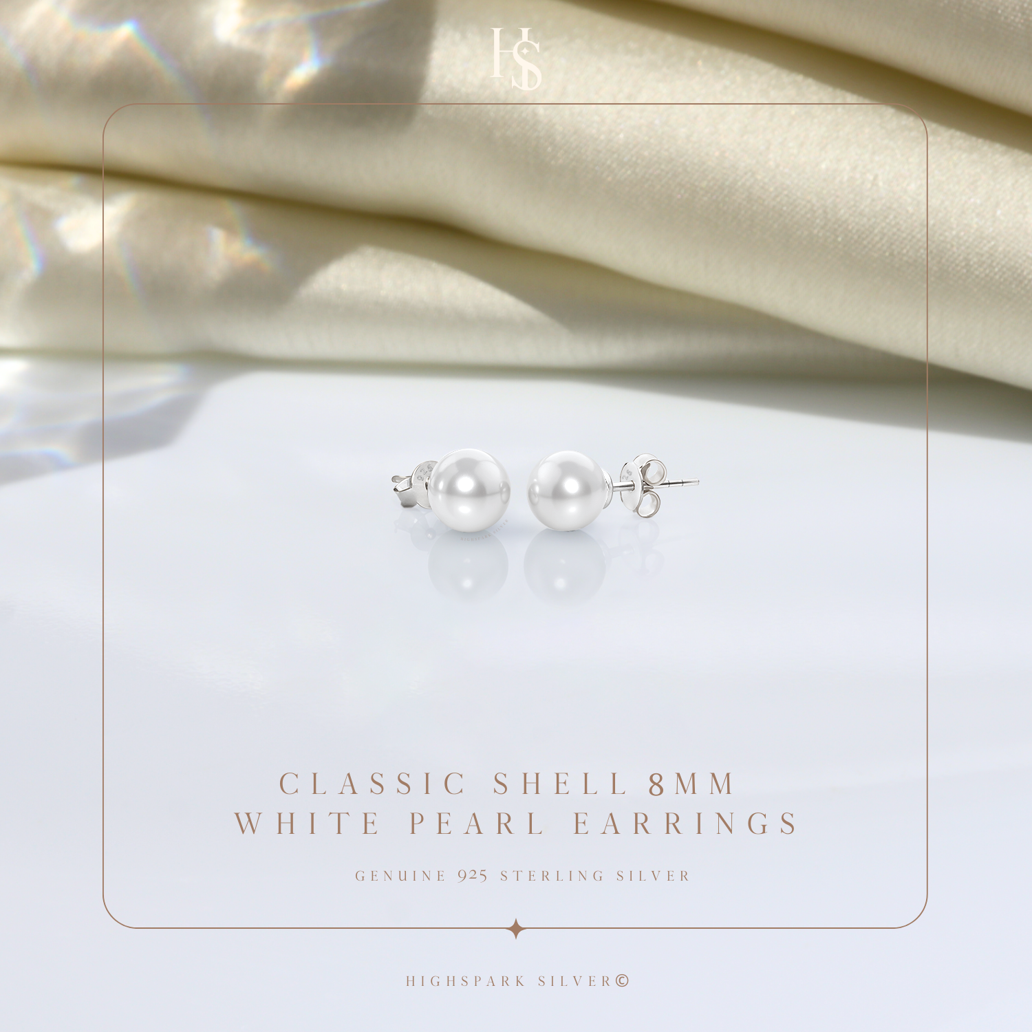 A pair of classic pearl stud earrings in sterling silver with push-back closures, styled on a reflective surface with draped cream satin.