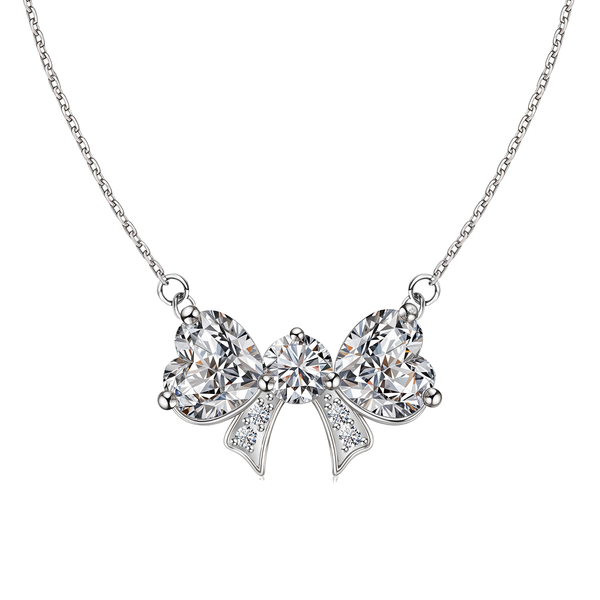 A sterling silver pendant necklace with a bow-shaped pendant made of two heart-cut and one round American diamond on a white background.