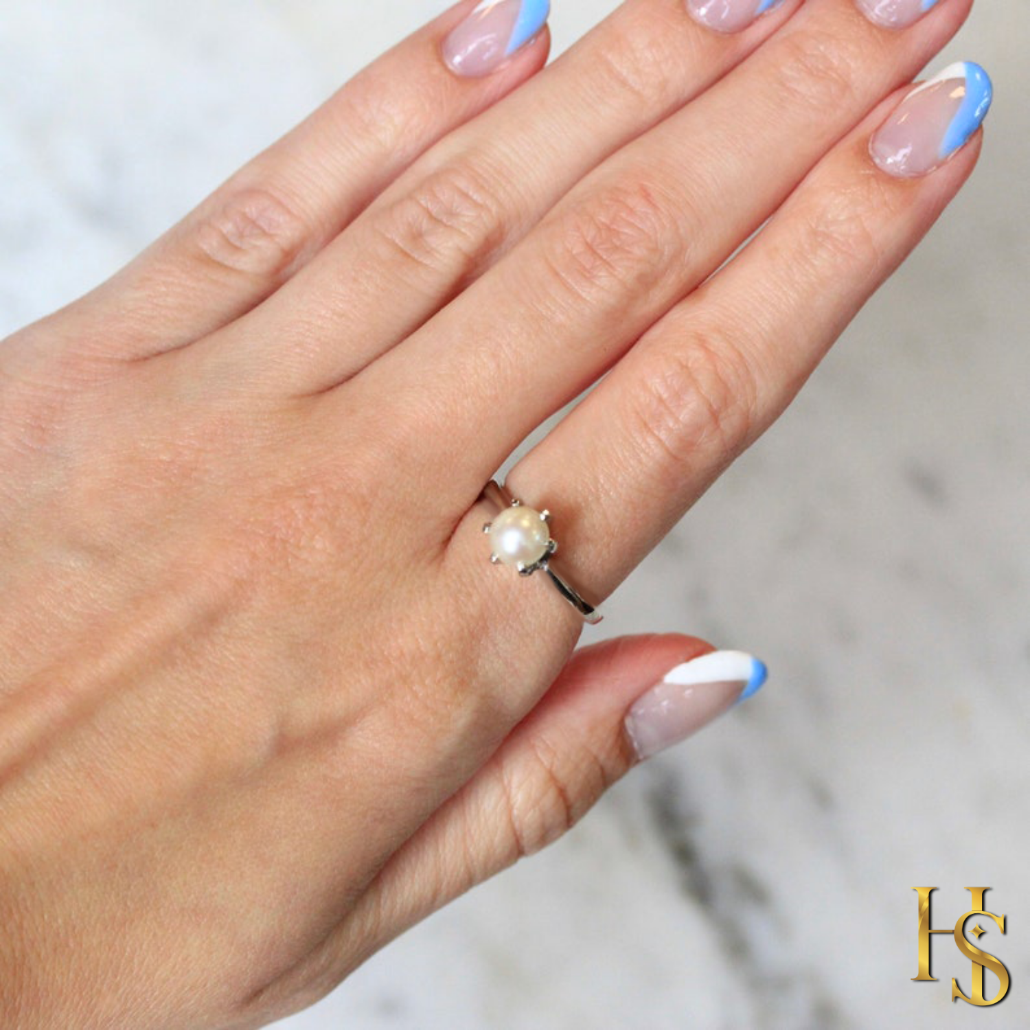 A solitaire pearl ring with a six-prong setting and a sterling silver band, worn on a hand with a blue and white manicure.